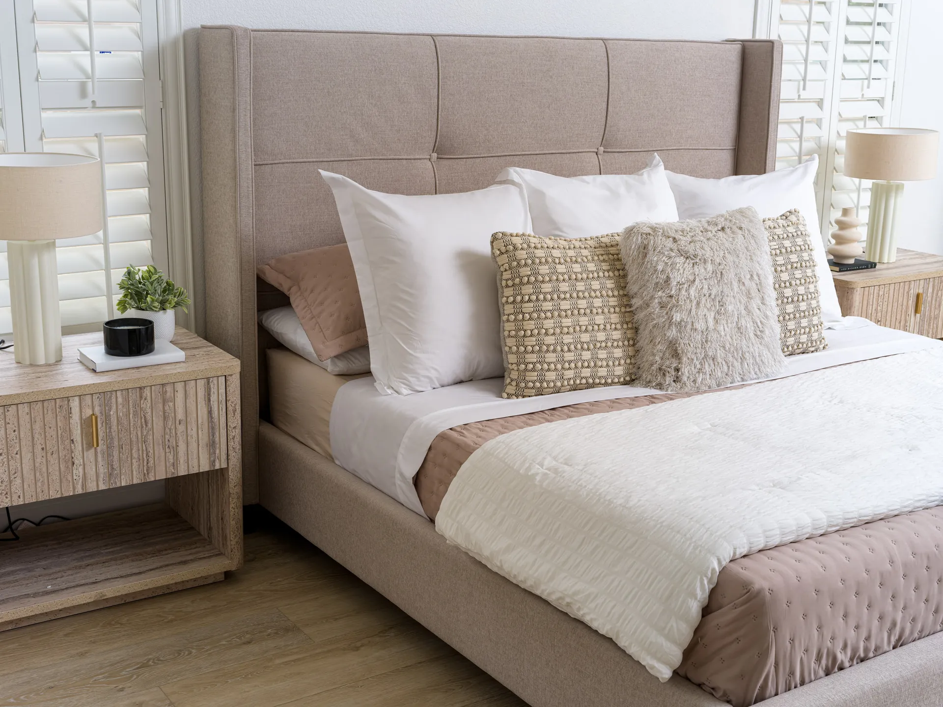 A neutral upholstered bed with layered pillows, matching nightstands, and cream lamps.