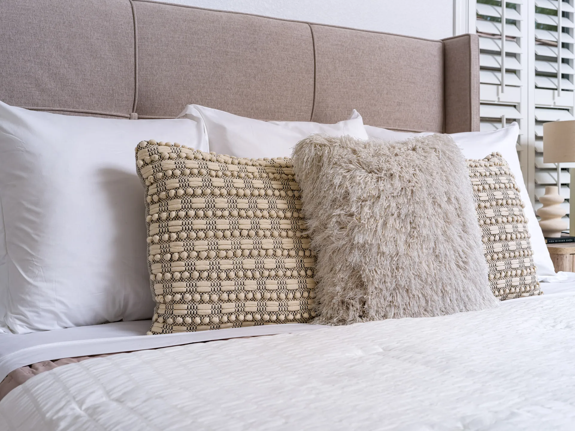 A neutral wingback headboard with layered pillows including a fluffy accent pillow.