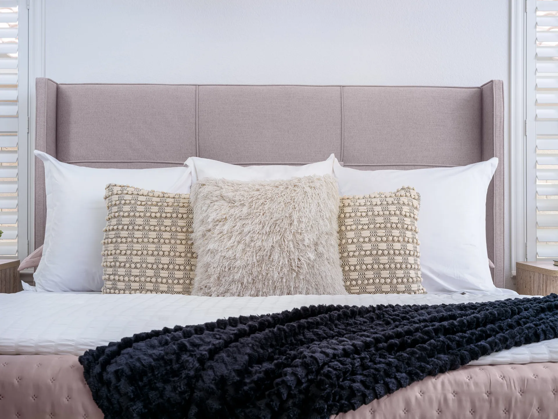 A soft, wingback-style headboard with layered neutral pillows and a plush black throw blanket.
