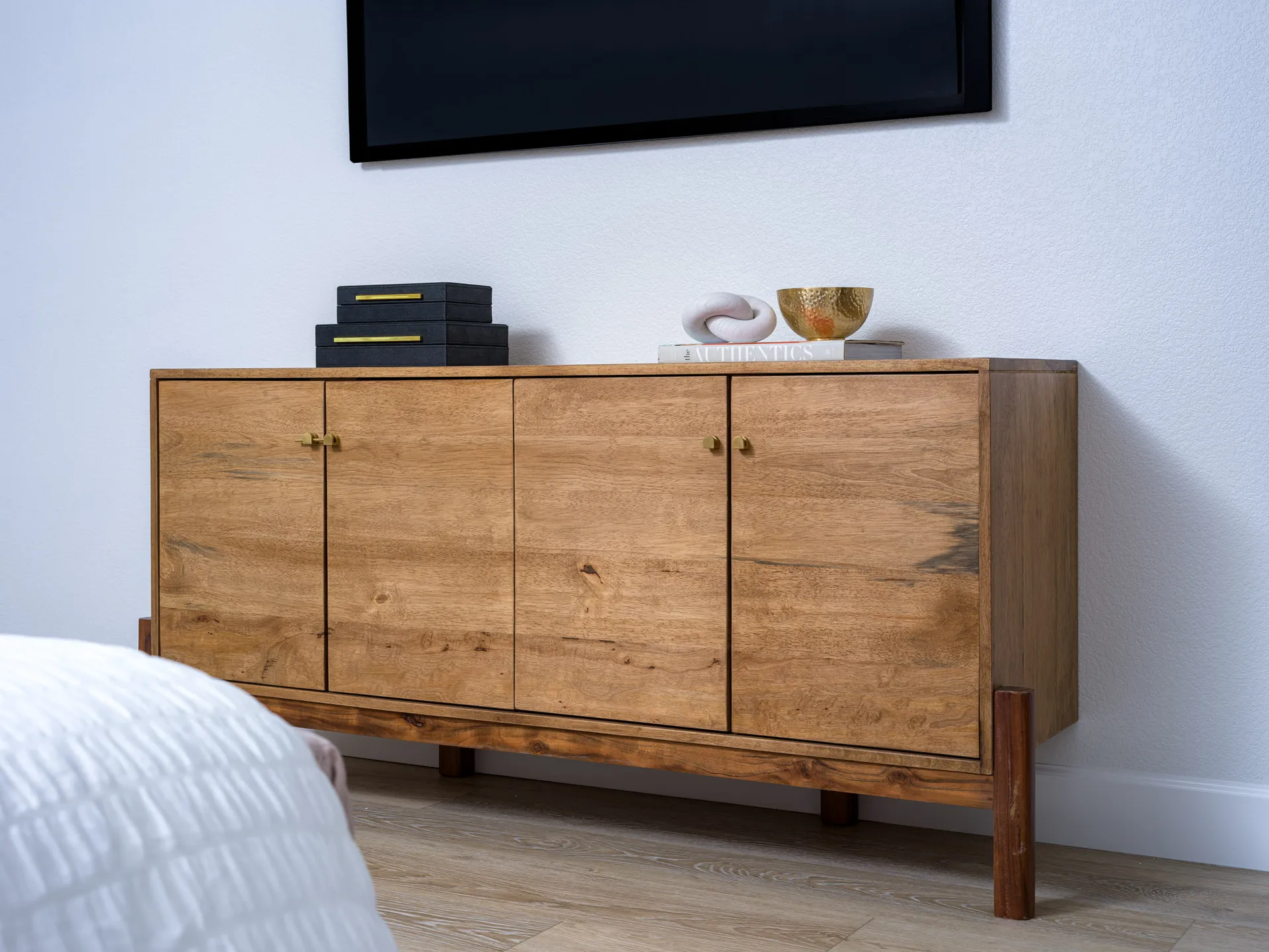 A wooden sideboard with gold hardware, topped by black boxes, a gold bowl, and a white sculpture.