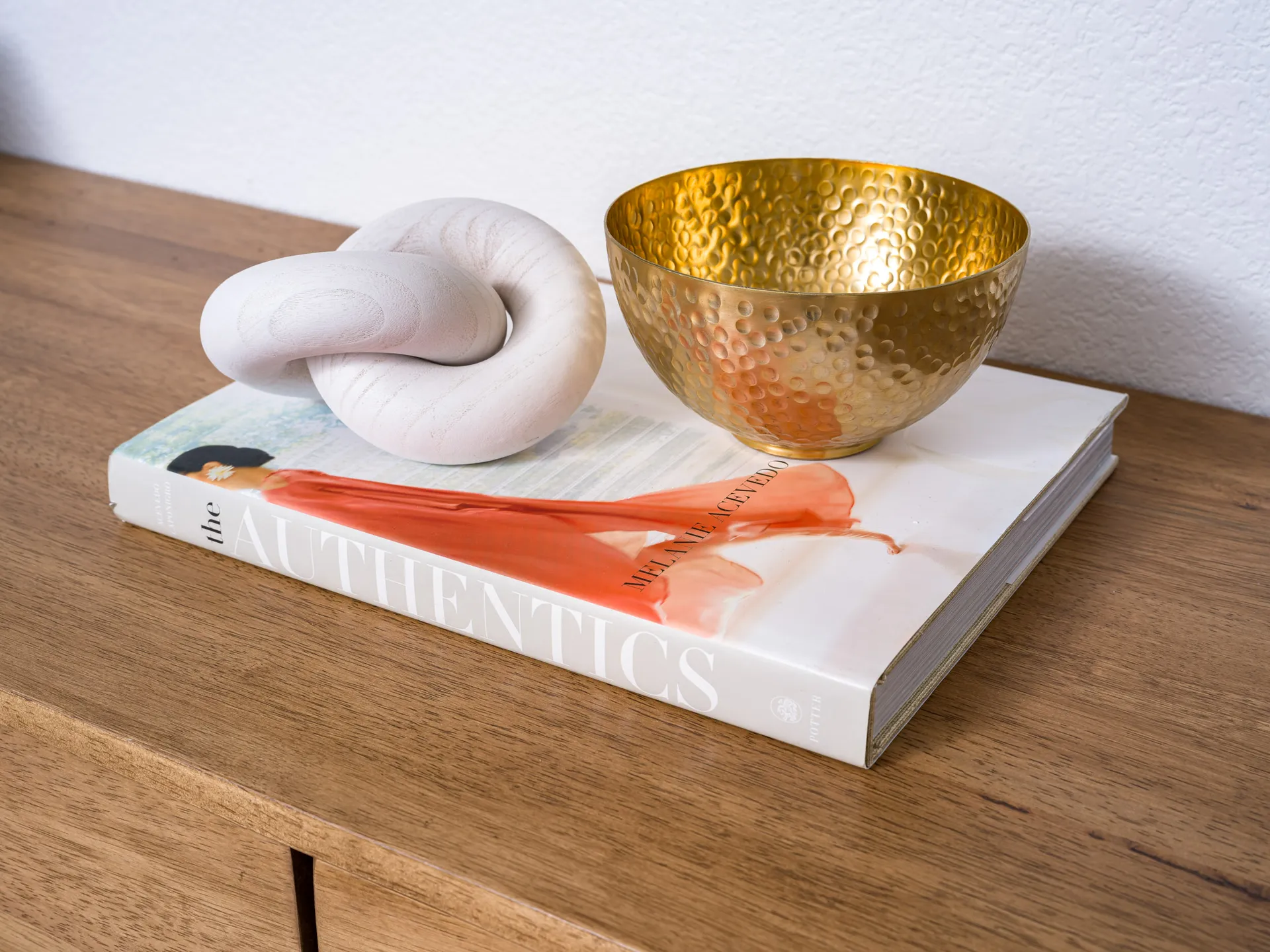 A hammered gold bowl and a white knot sculpture on a hardcover book.