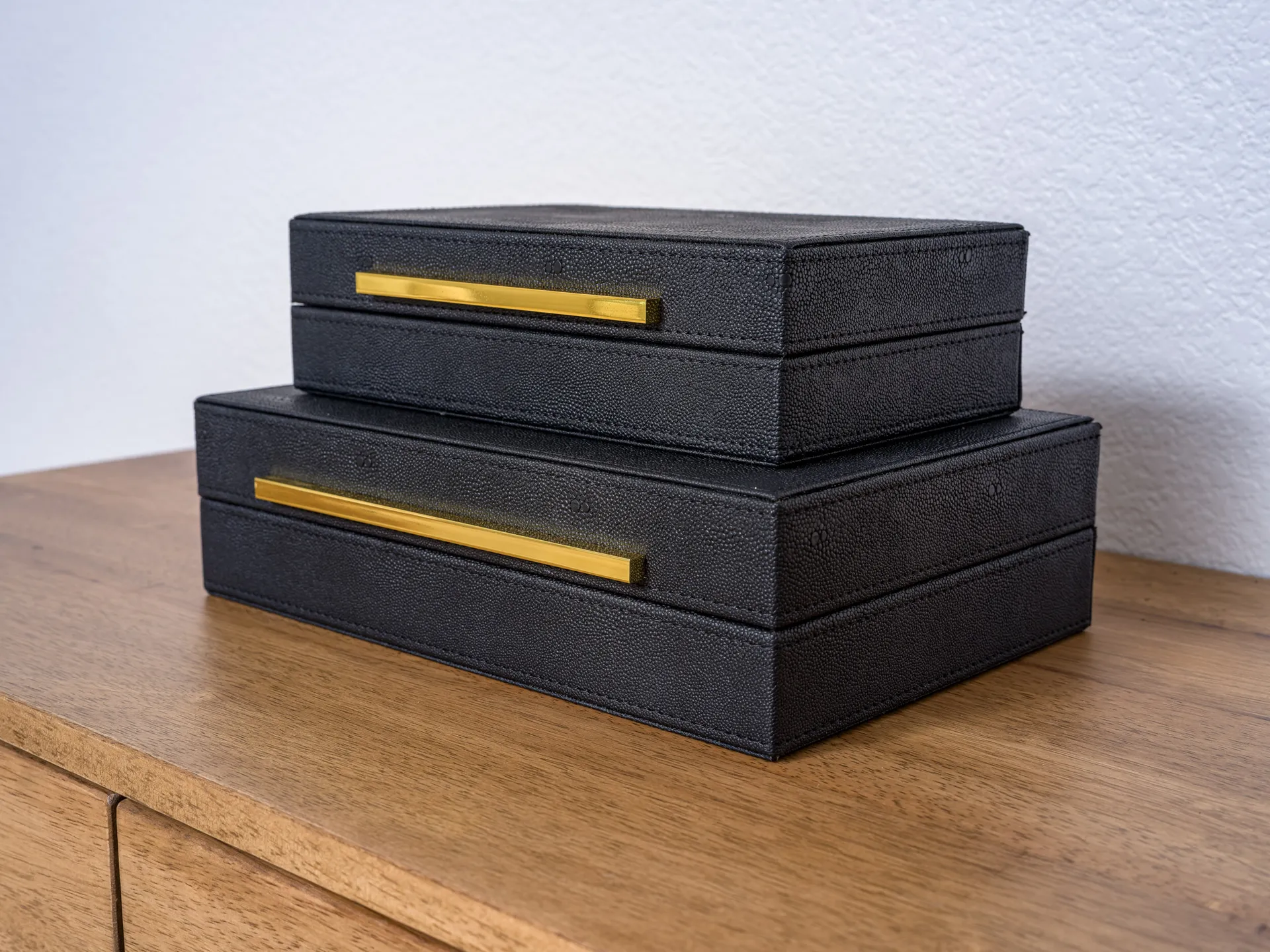 Two black rectangular boxes with gold handles stacked on a wooden surface.