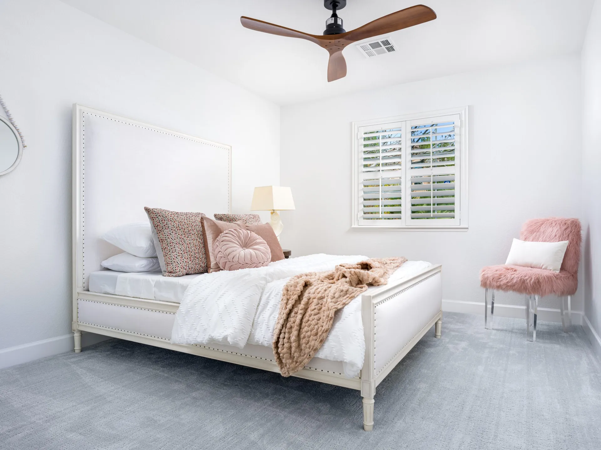 Modern bedroom with white bed, pink accents, and a minimalist design featuring a ceiling fan and neutral color palette
