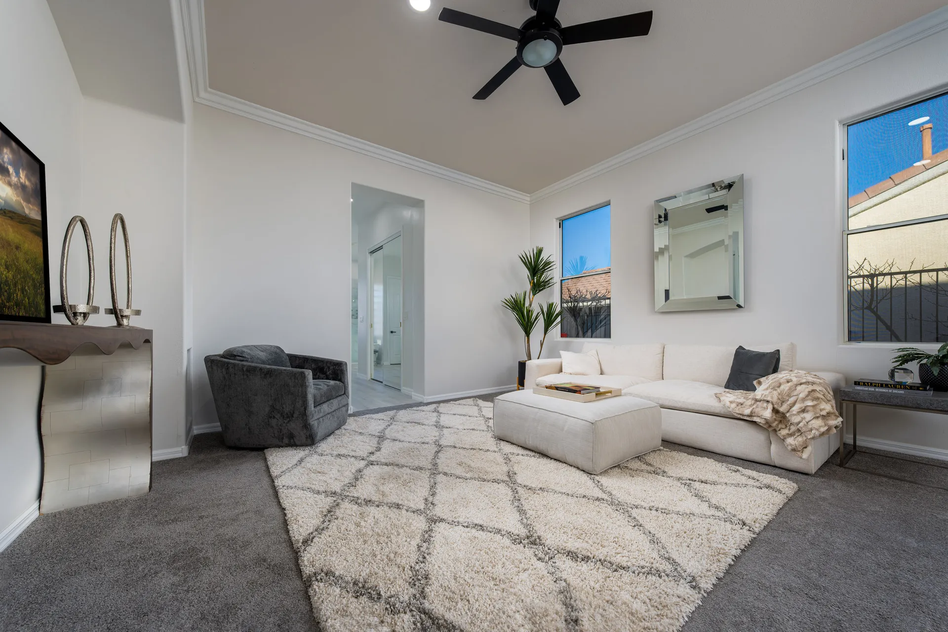 A serene bedroom sitting area with a white sectional, plush ottoman, textured area rug, and modern decor."