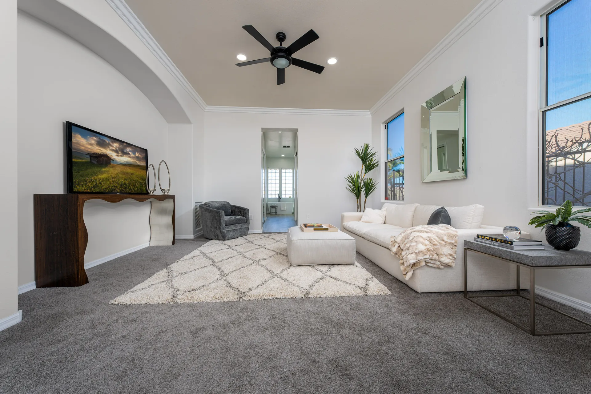 A serene bedroom lounge with a white sofa, plush ottoman, sculptural console table, and modern decor, creating a cozy and stylish retreat.