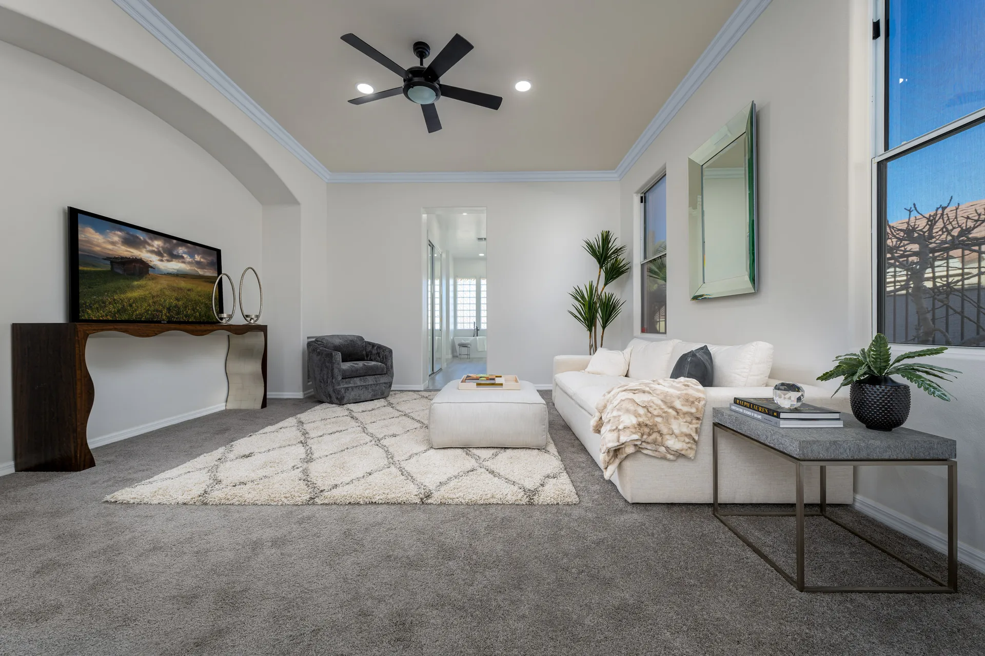 A spacious bedroom lounge with a plush white sofa, textured area rug, sculptural console table, and elegant decor.