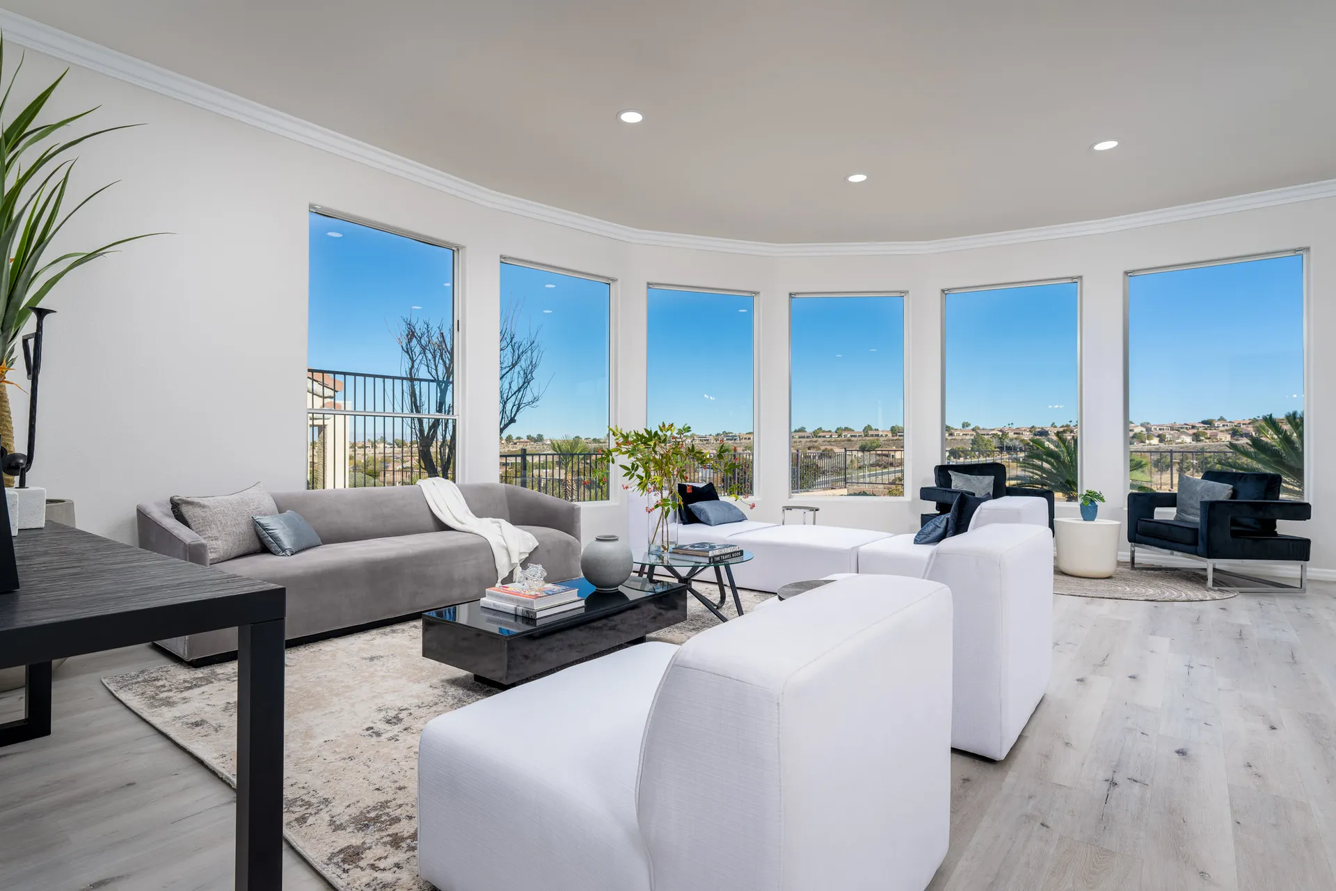 A contemporary living room with a gray sofa, white lounge chairs, a black coffee table, and floor-to-ceiling windows showcasing stunning views.