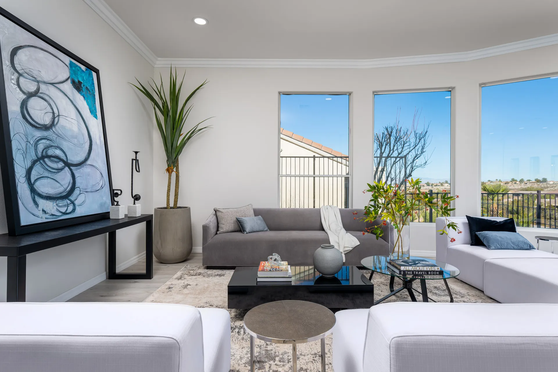 A contemporary living room with a sleek gray sofa, white lounge chairs, abstract artwork, and floor-to-ceiling windows showcasing panoramic views.