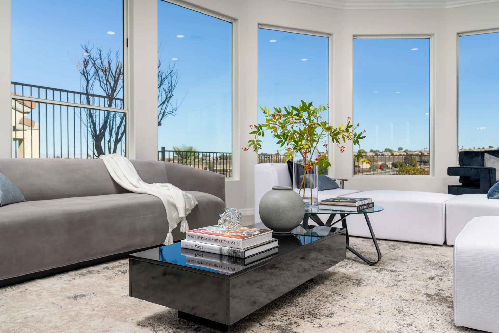 A contemporary living room with a plush gray sofa, black coffee table, modern decor, and large windows showcasing scenic outdoor views.