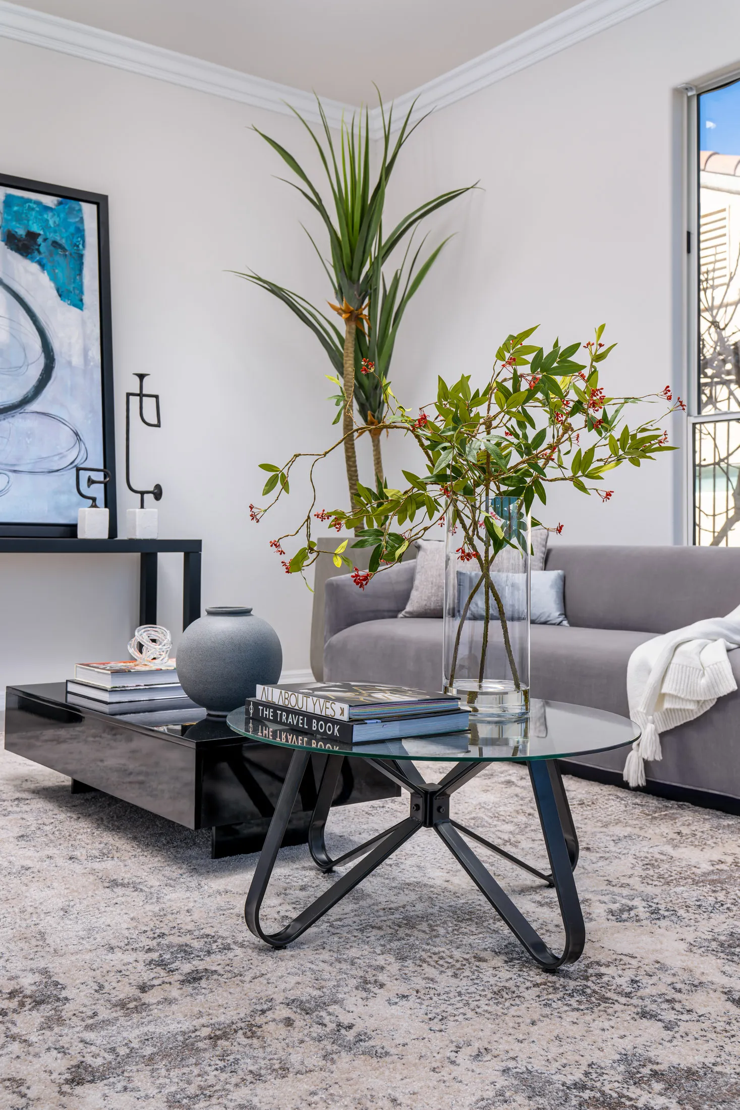 A contemporary living room with a glass coffee table, a sleek gray sofa, abstract artwork, and elegant decor accents.
