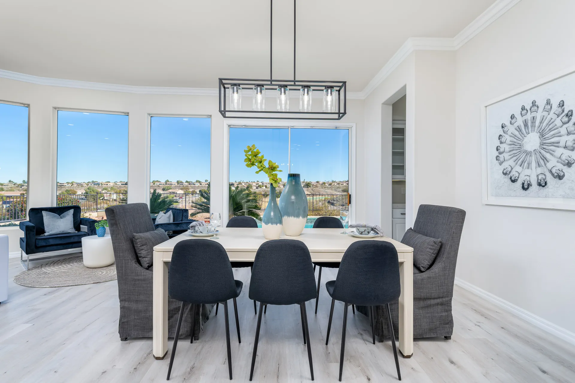 A modern dining room with a white wood table, dark upholstered chairs, large windows showcasing panoramic views, and elegant blue vases as decor.