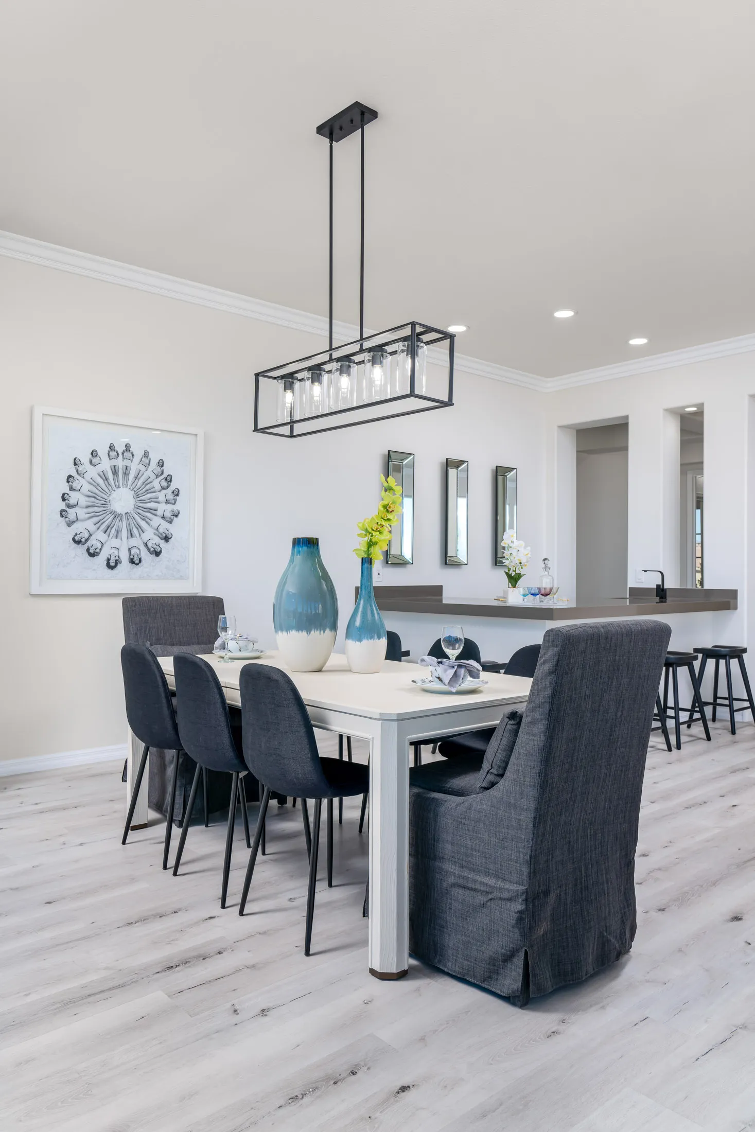 A modern dining room with a white wood table, dark upholstered chairs, blue decorative vases, and a sleek open-concept layout.