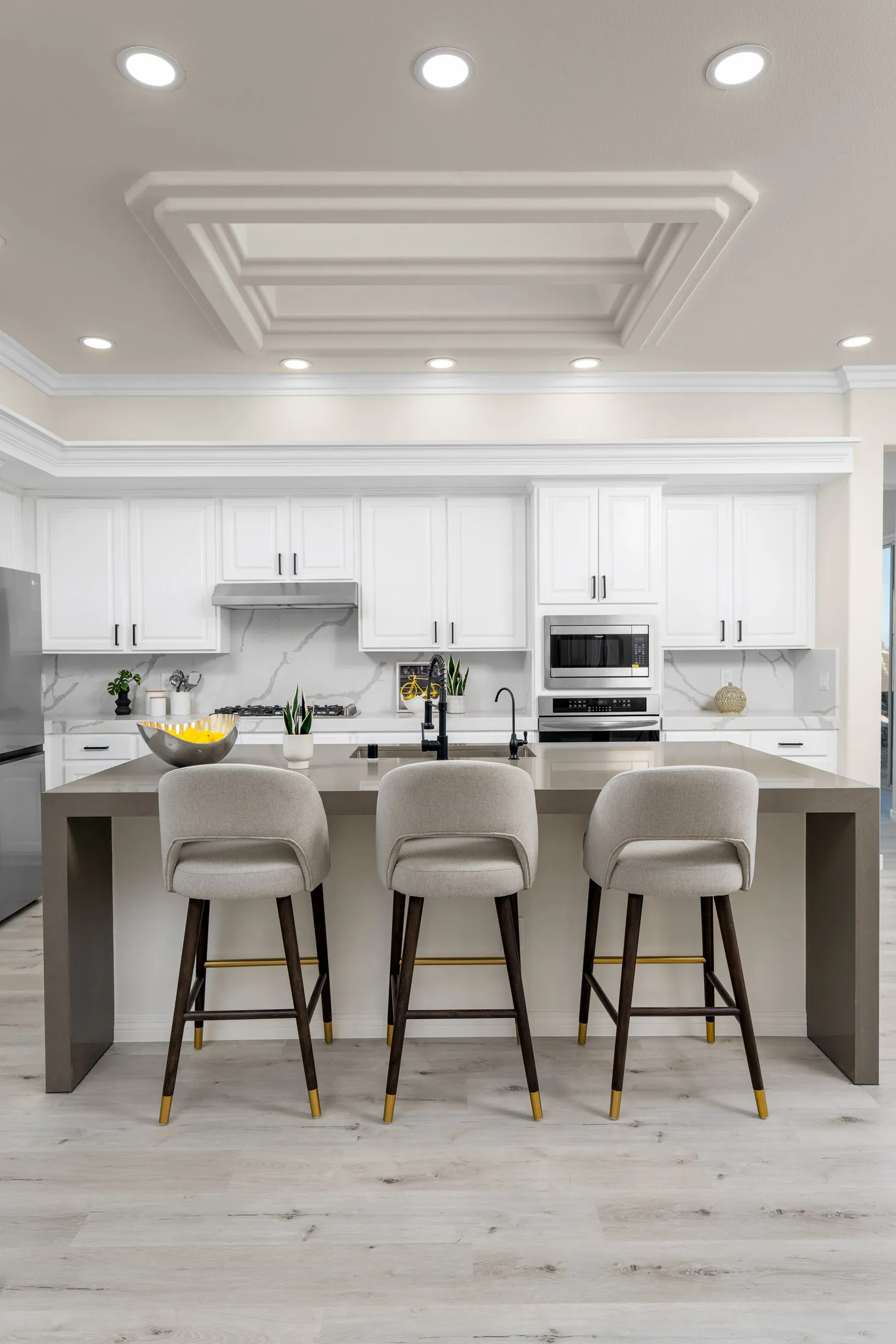 A sleek kitchen with a large island, upholstered barstools, white cabinetry, and marble backsplash for a contemporary look.