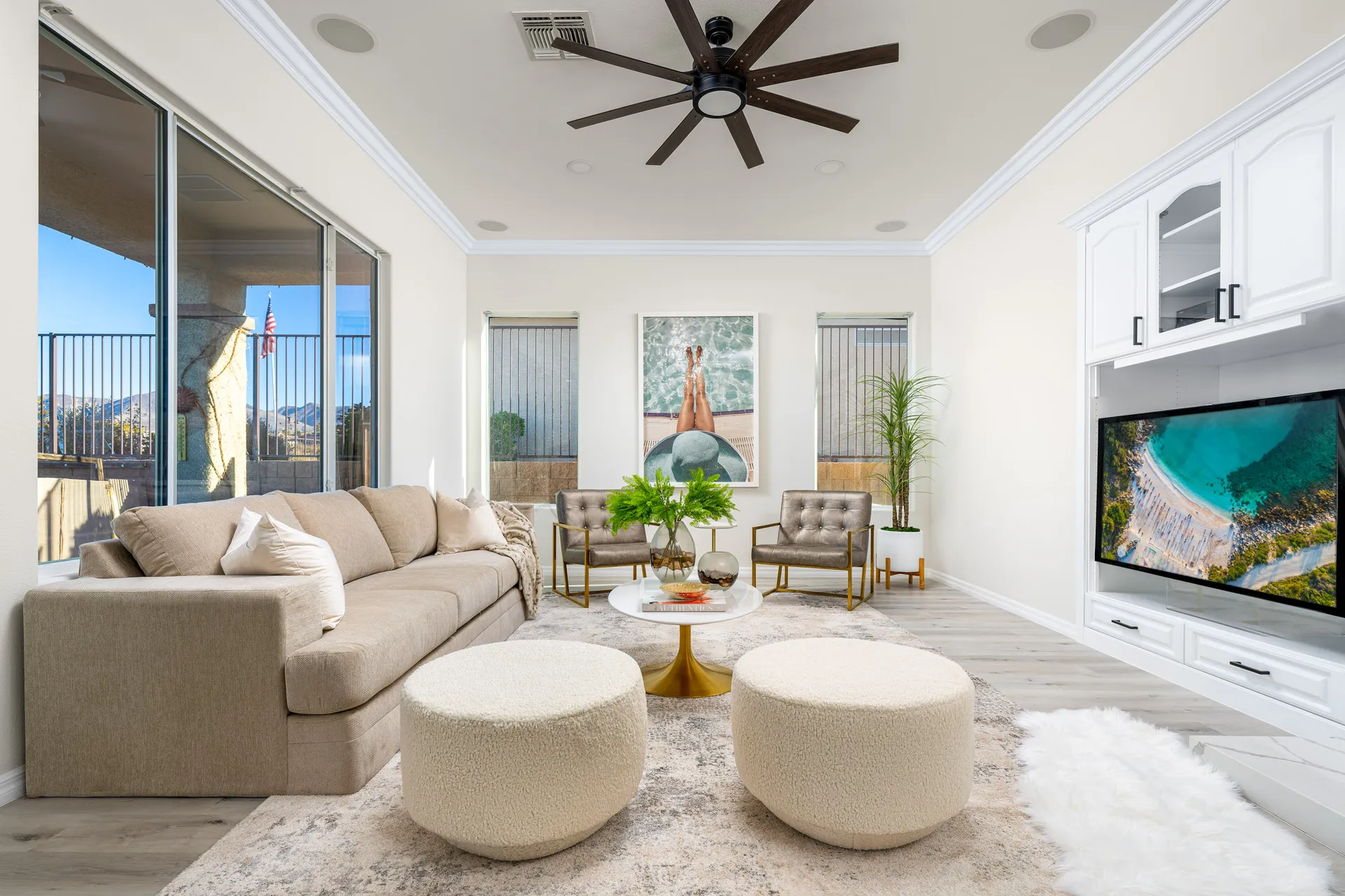 A modern living room with a neutral-toned sectional, boucle ottomans, gold-accented chairs, and large windows bringing in natural light.