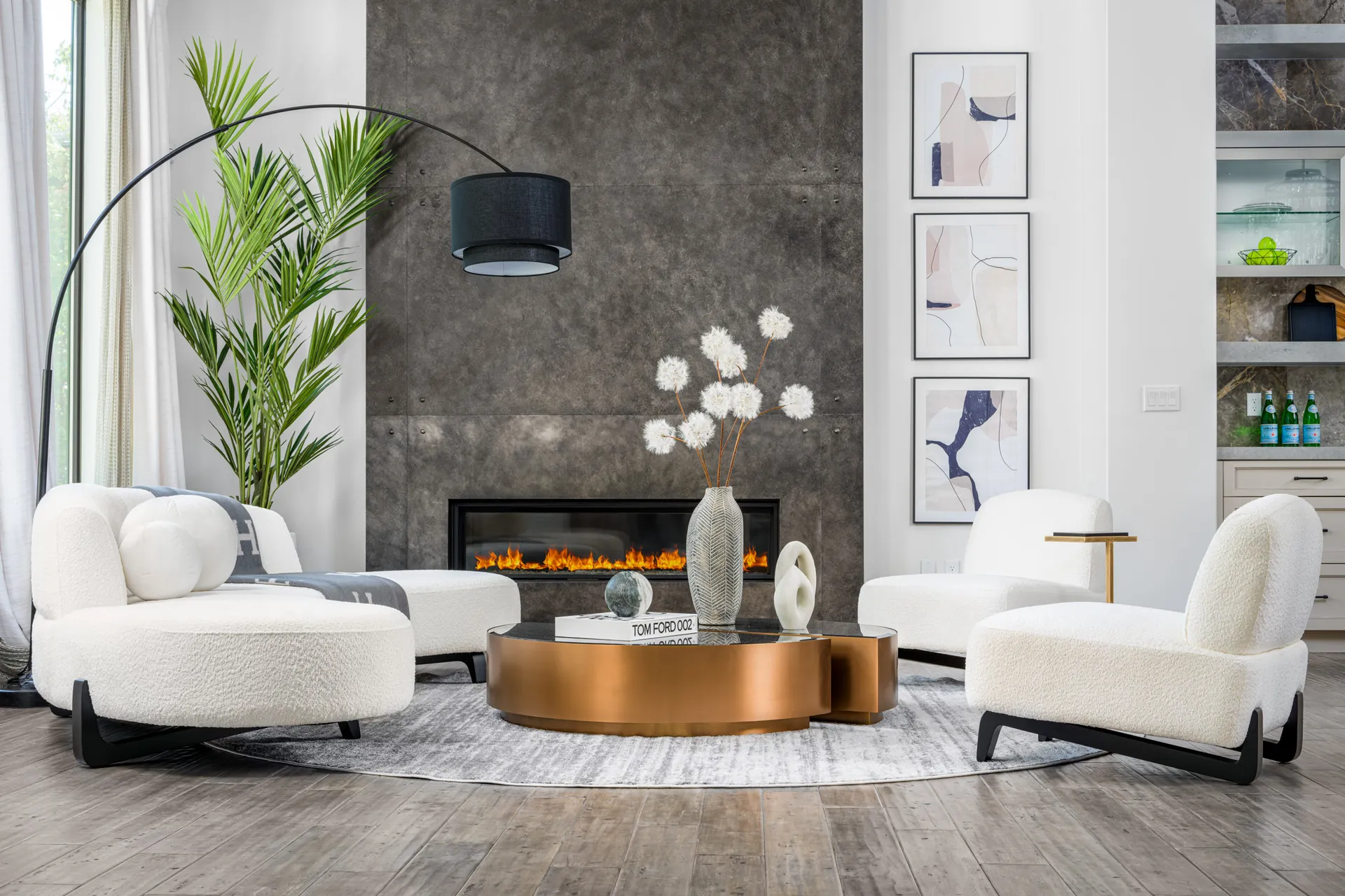 Stylish living room setup featuring a bronze coffee table, plush white chairs, a modern arc lamp, and an accent fireplace with a textured wall. A refined example of Modern Luxury Home Staging by Stately.