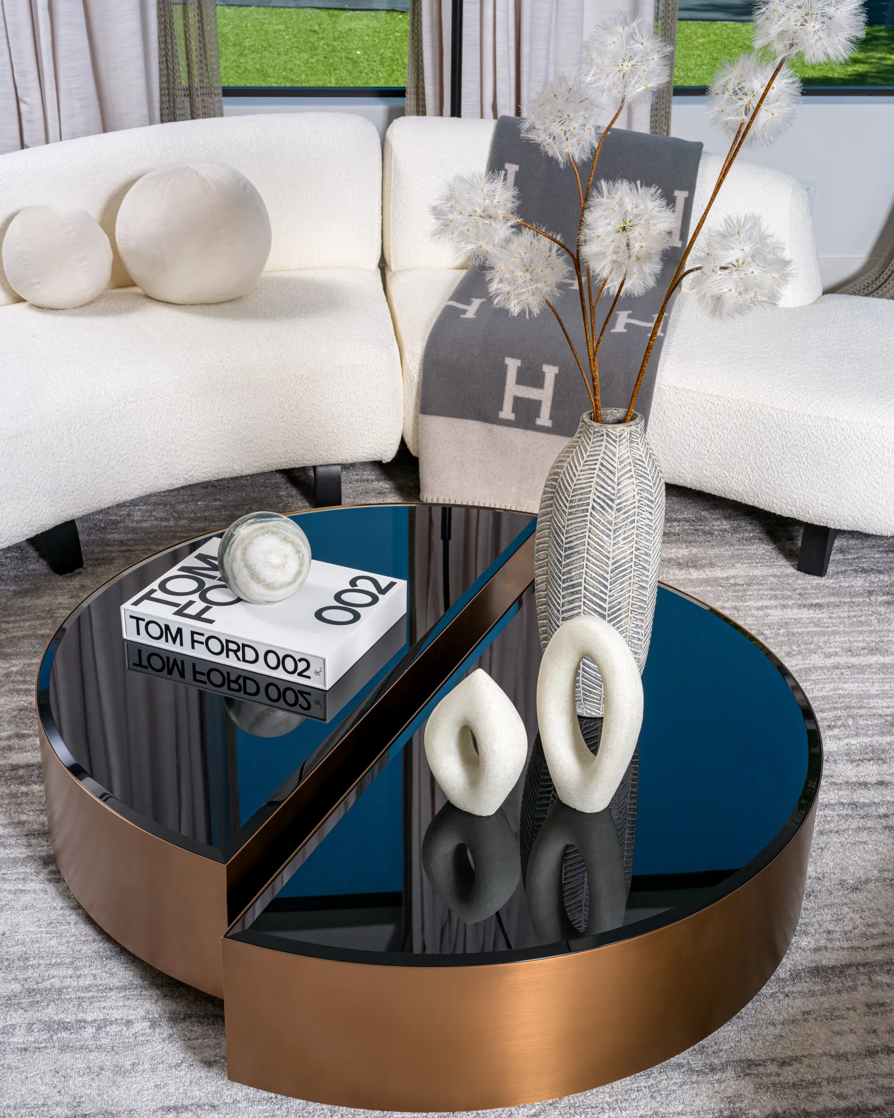 A sleek round coffee table with a bronze finish and black glass top, styled with modern decor including a textured vase, sculptural accents, and a designer book. This design reflects Stately’s expertise in creating elegant interiors through luxury home staging in Las Vegas.