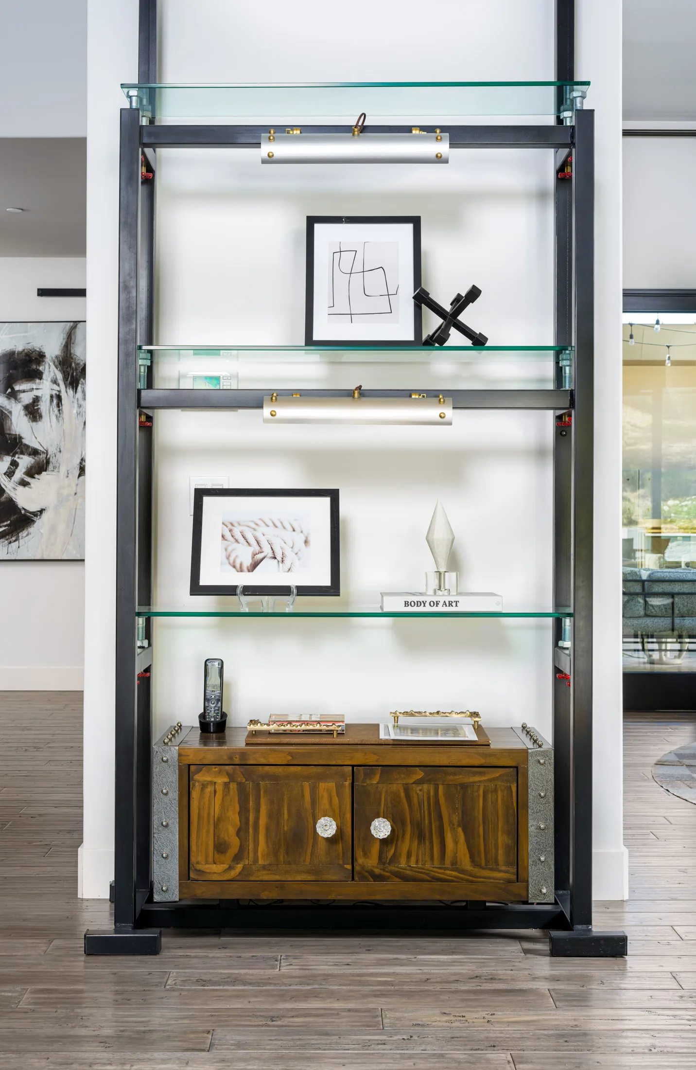 A modern display shelf featuring glass shelves with framed artwork, decorative objects, and books, paired with a wooden cabinet base. This design showcases Stately’s meticulous attention to detail in luxury home staging and interior design in Las Vegas.