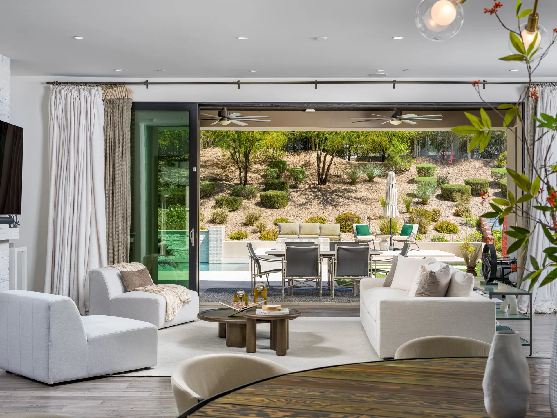 A stylish living room with modern seating and a warm wood coffee table, opening to an outdoor patio and landscaped yard with lounge seating. This design highlights Stately’s luxury home staging expertise in Las Vegas, blending comfort and elegance.