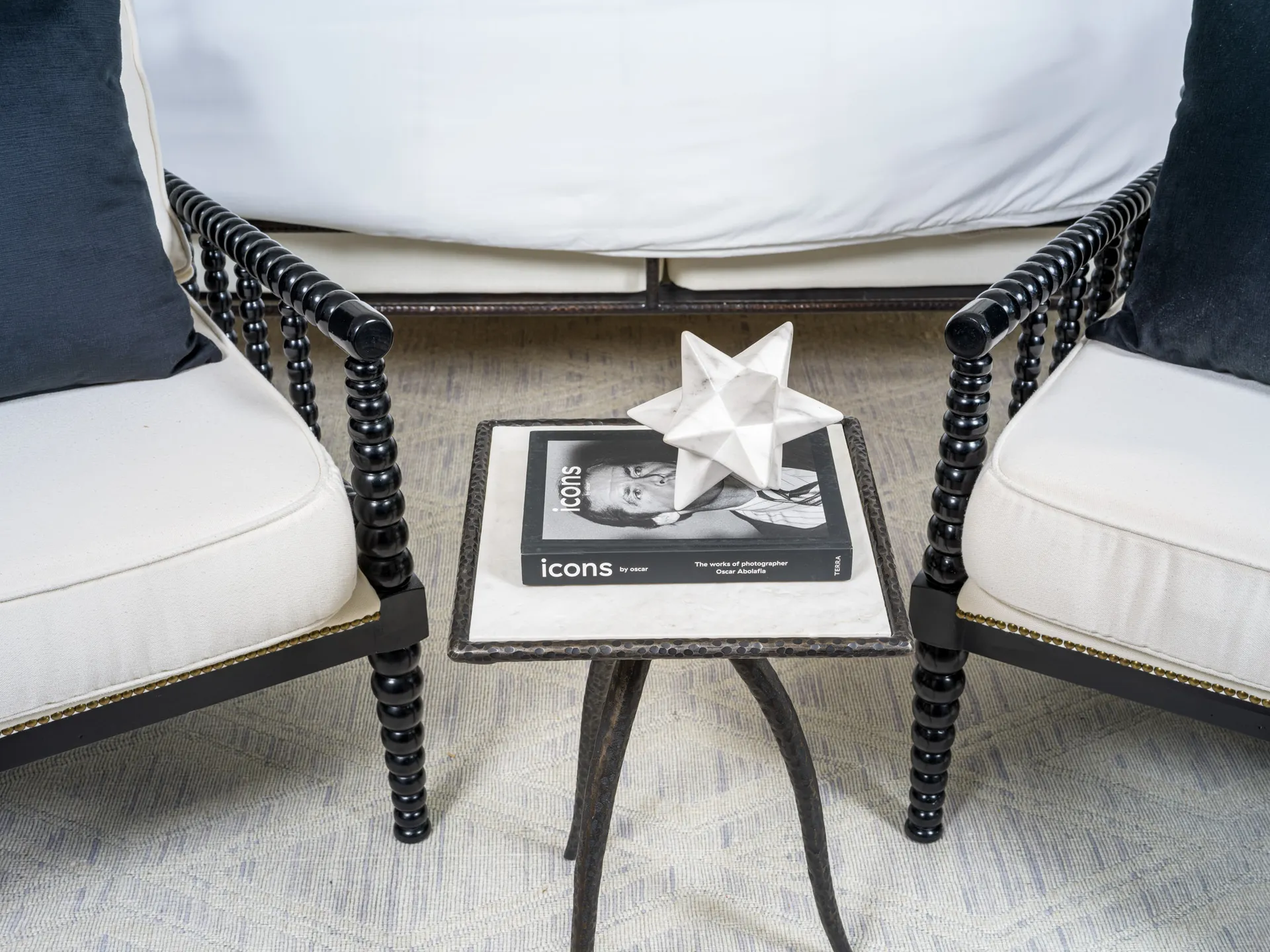 A close-up of a stylish side table with a marble top and hammered metal edges, adorned with a modern star sculpture and a design book, flanked by elegant black spindle chairs. This setup highlights Stately’s attention to detail in luxury home staging and interior design in Las Vegas.