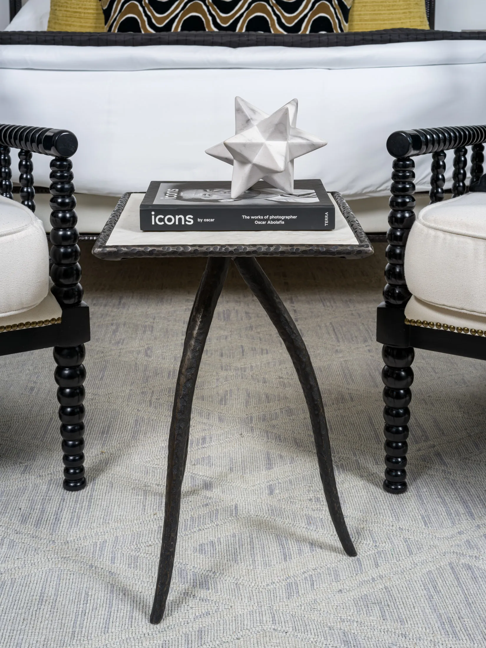 A close-up of a hammered metal side table styled with a modern geometric star sculpture and a designer book, flanked by elegant spindle chairs, showcasing the meticulous attention to detail in Stately’s luxury home staging and interior design in Las Vegas.