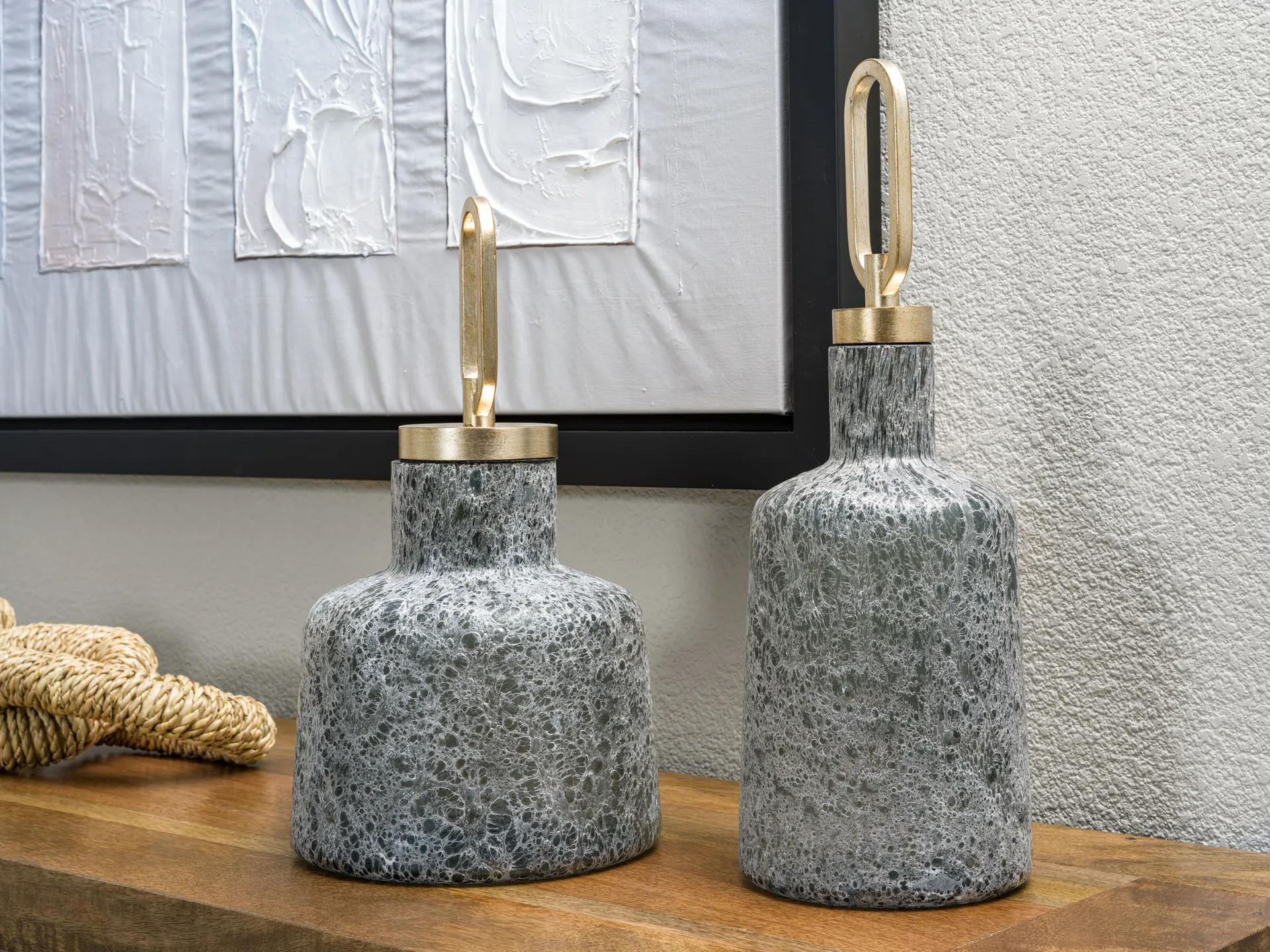 Two gray, textured decorative vases with gold loop handles on a wooden console.