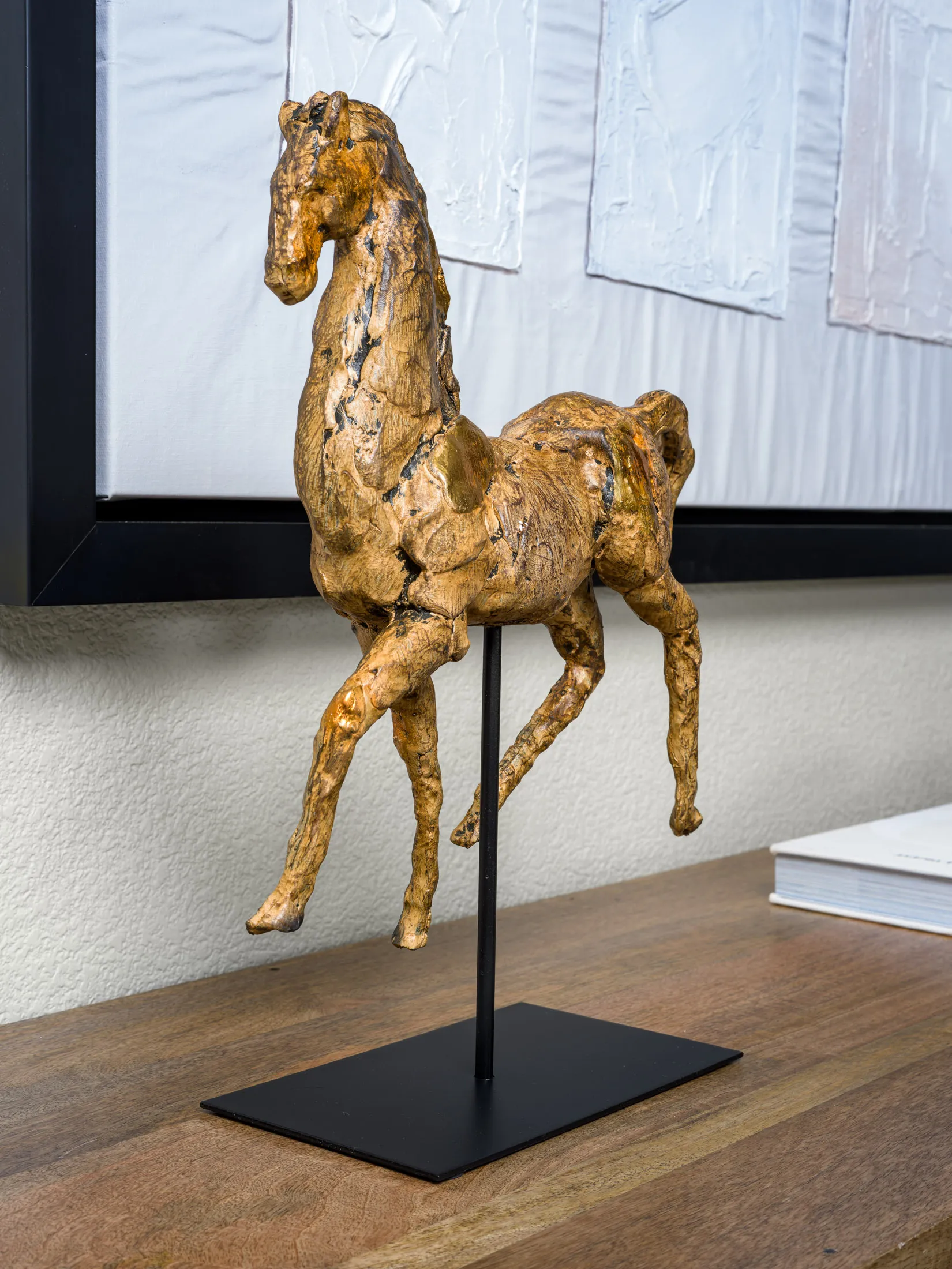 A close-up of a textured gold horse sculpture mounted on a black stand.