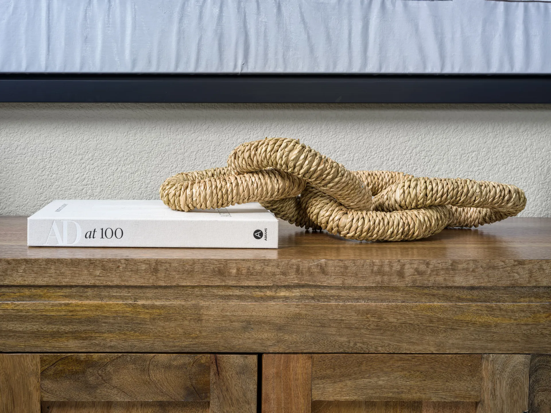 A coiled woven rope accent resting on a white coffee table book atop a wooden console.