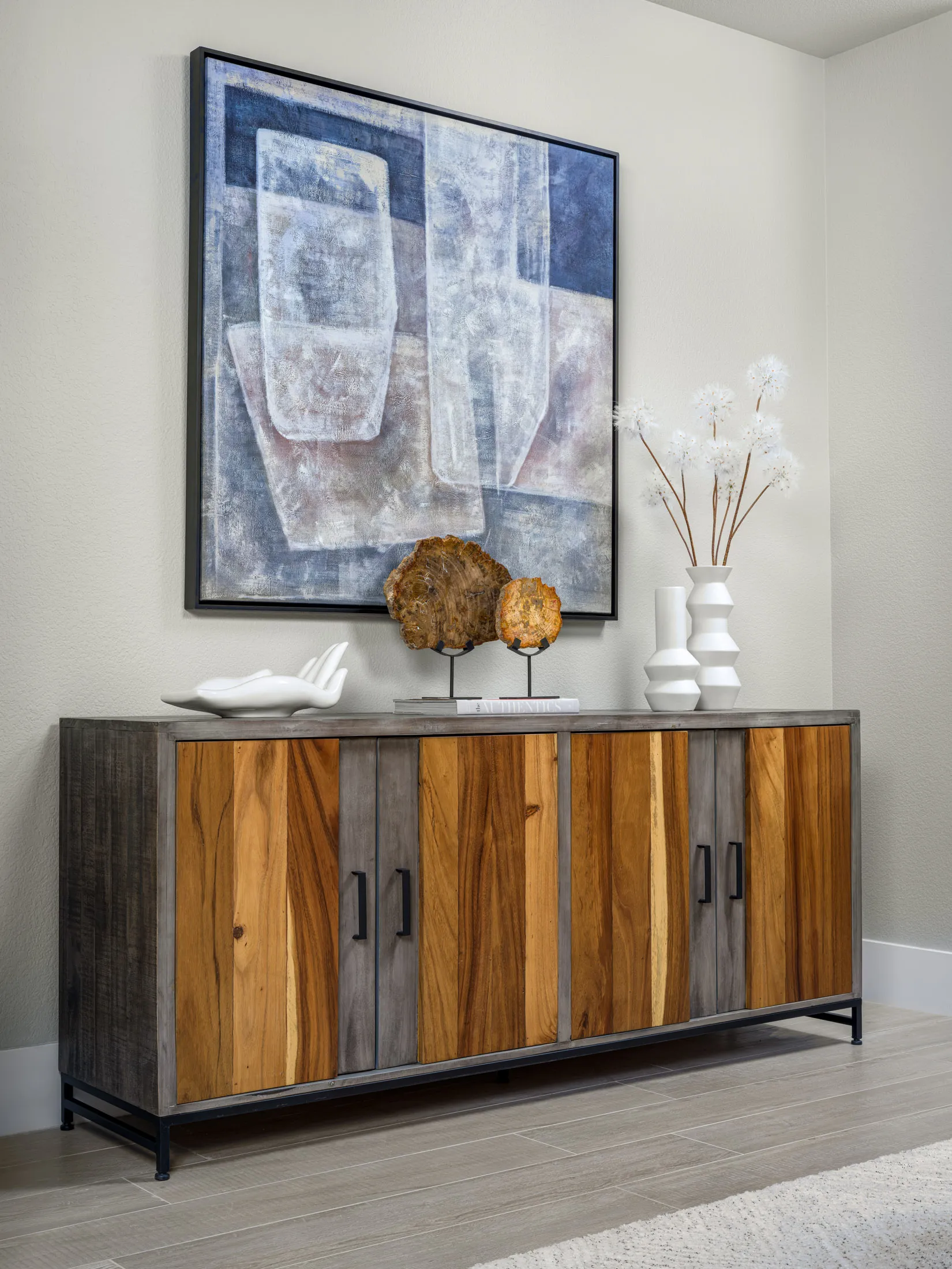 A multi-toned wooden console with decorative items and a large abstract painting on the wall.