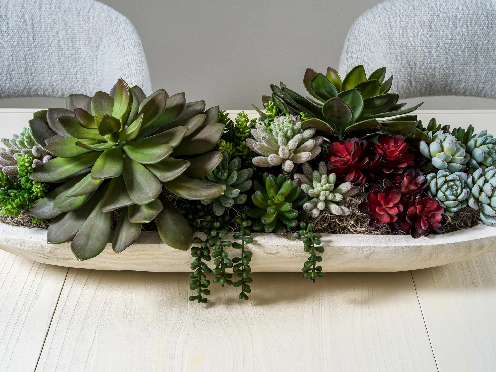 A decorative arrangement of green and red succulents in a wooden bowl.