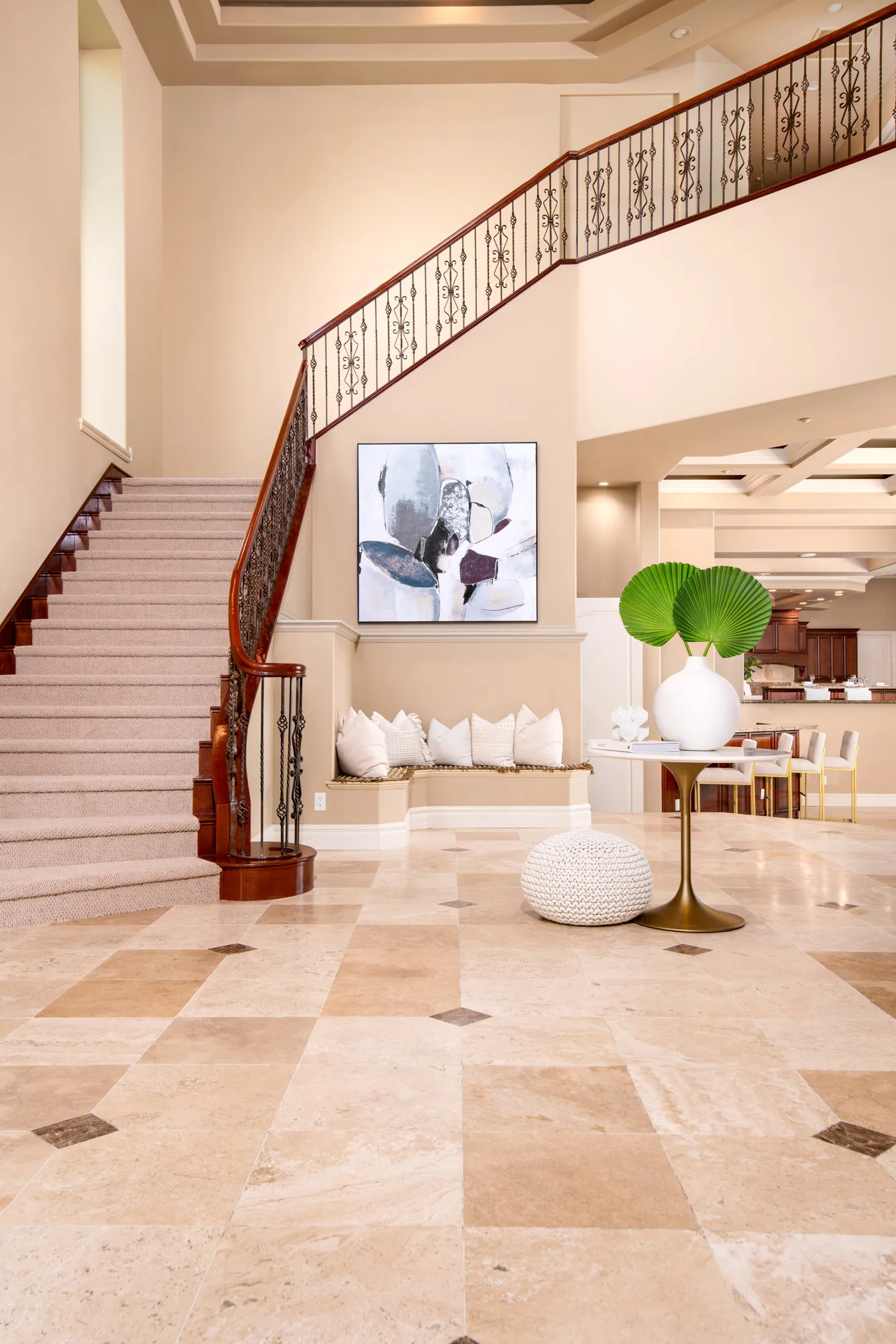 A tall foyer showcasing a curved wooden staircase with wrought-iron railings, a built-in bench with white pillows, and a round accent table.