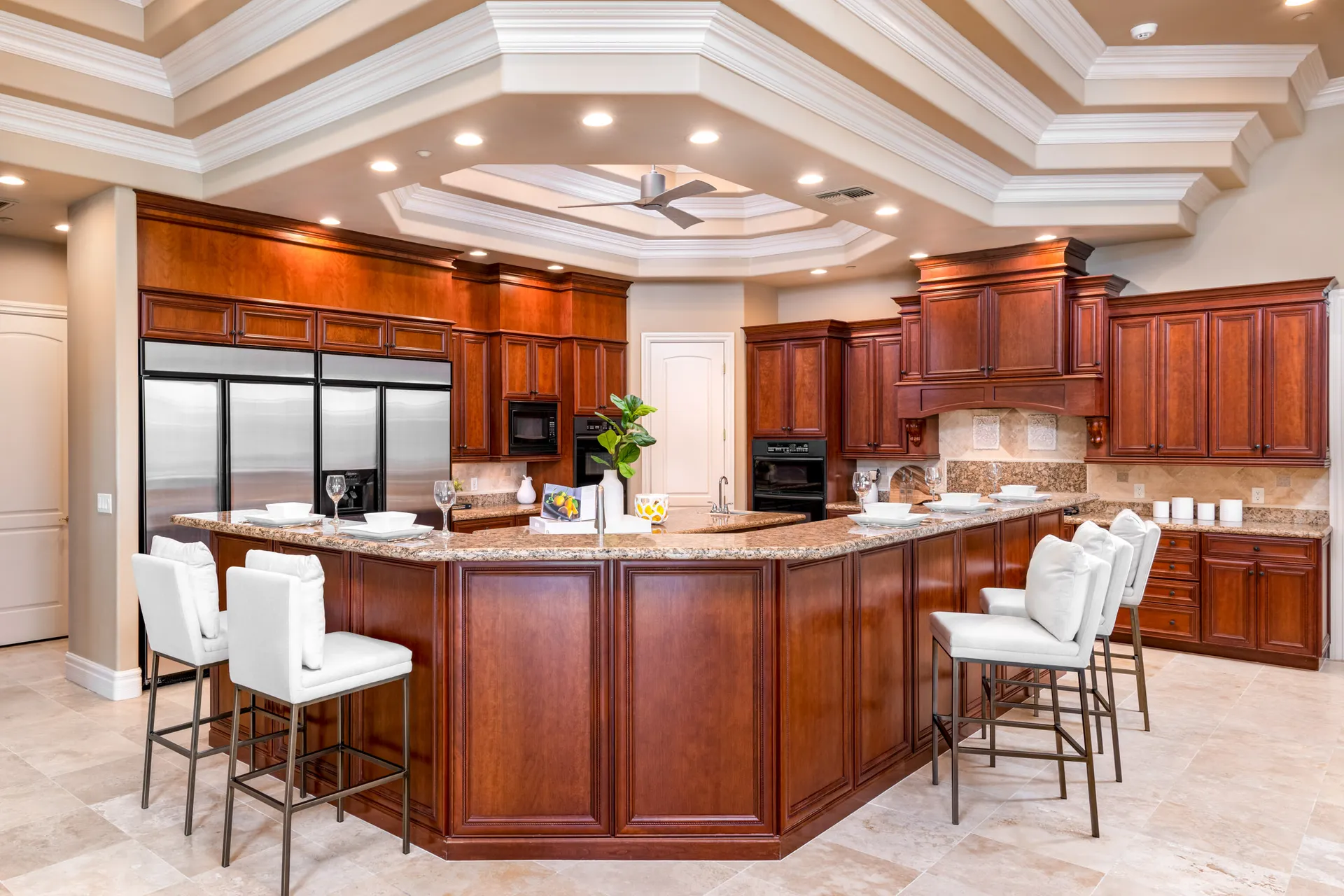 A spacious kitchen with cherry wood cabinets, a large granite-topped island, and white bar stools under a coffered ceiling.