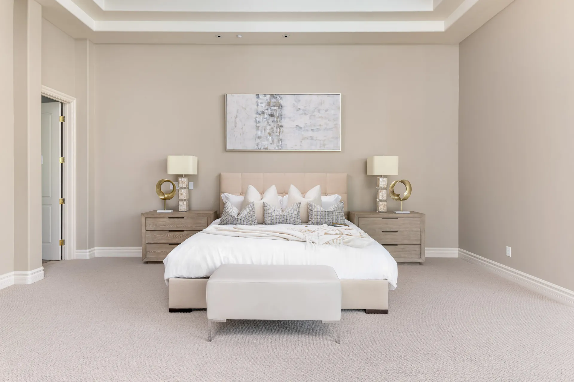 A large upholstered bed with neutral bedding, matching wooden nightstands, and a bench at the foot.