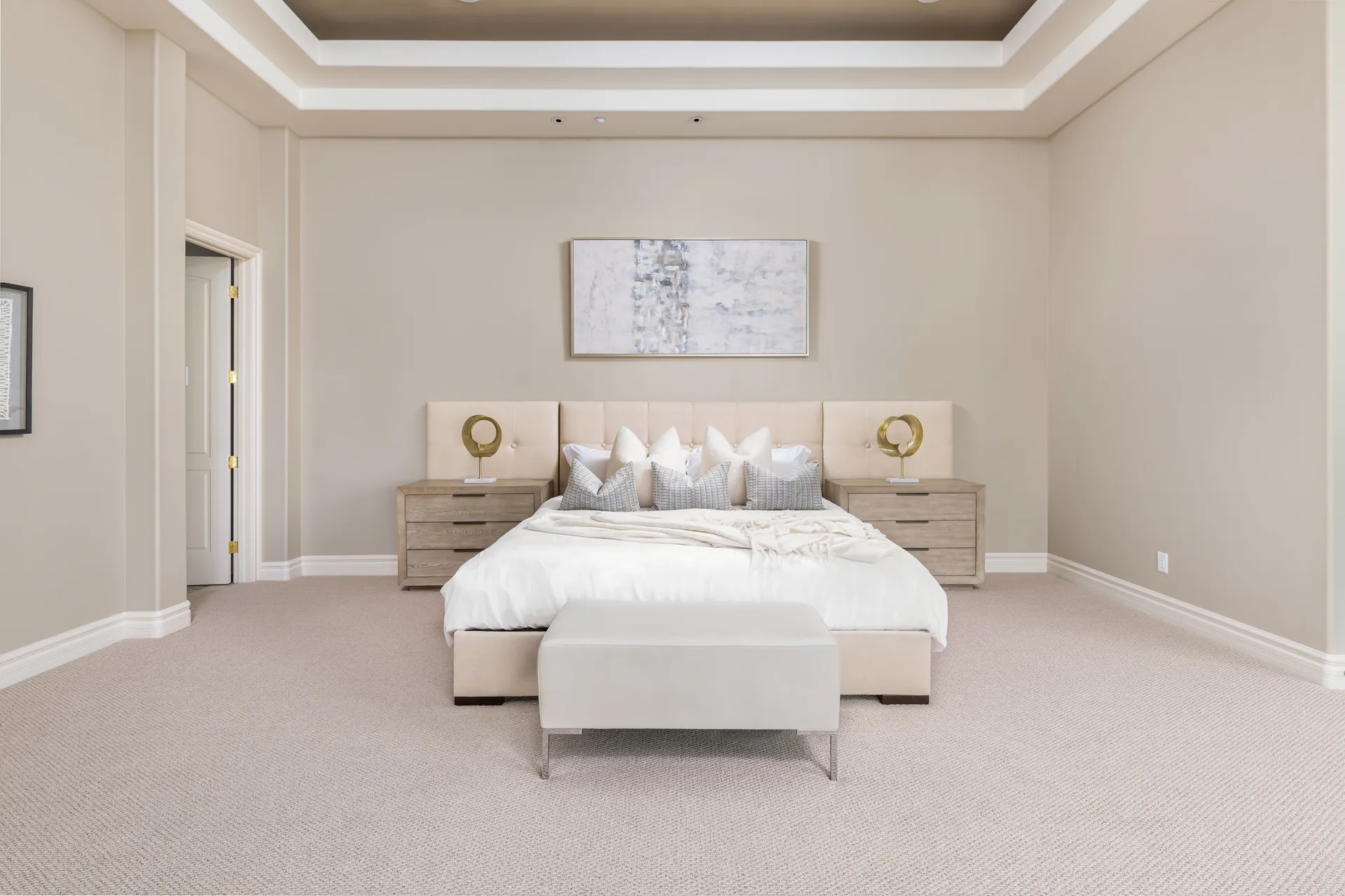 A spacious bedroom with a tufted headboard, neutral bedding, matching nightstands, and a bench at the foot of the bed.