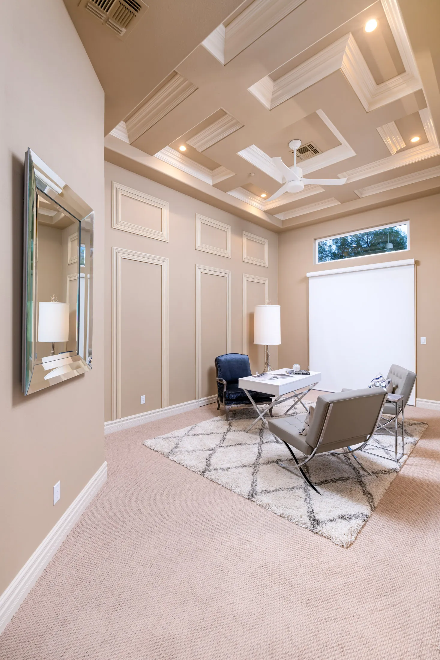 A lounge featuring an intricate coffered ceiling, a navy velvet chair, modern accent chairs, a white desk, and a plush rug in neutral tones.
