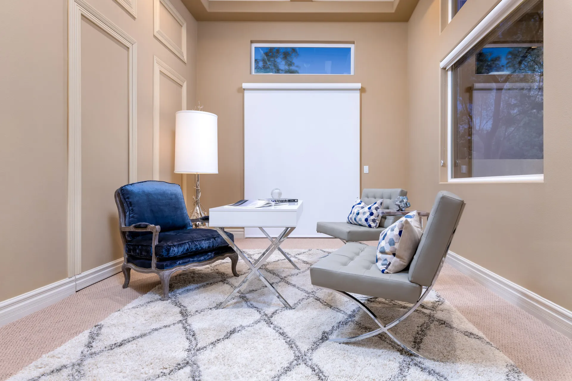 A small sitting area with a plush navy velvet chair, modern tufted chairs, a white accent table, and a tall floor lamp.