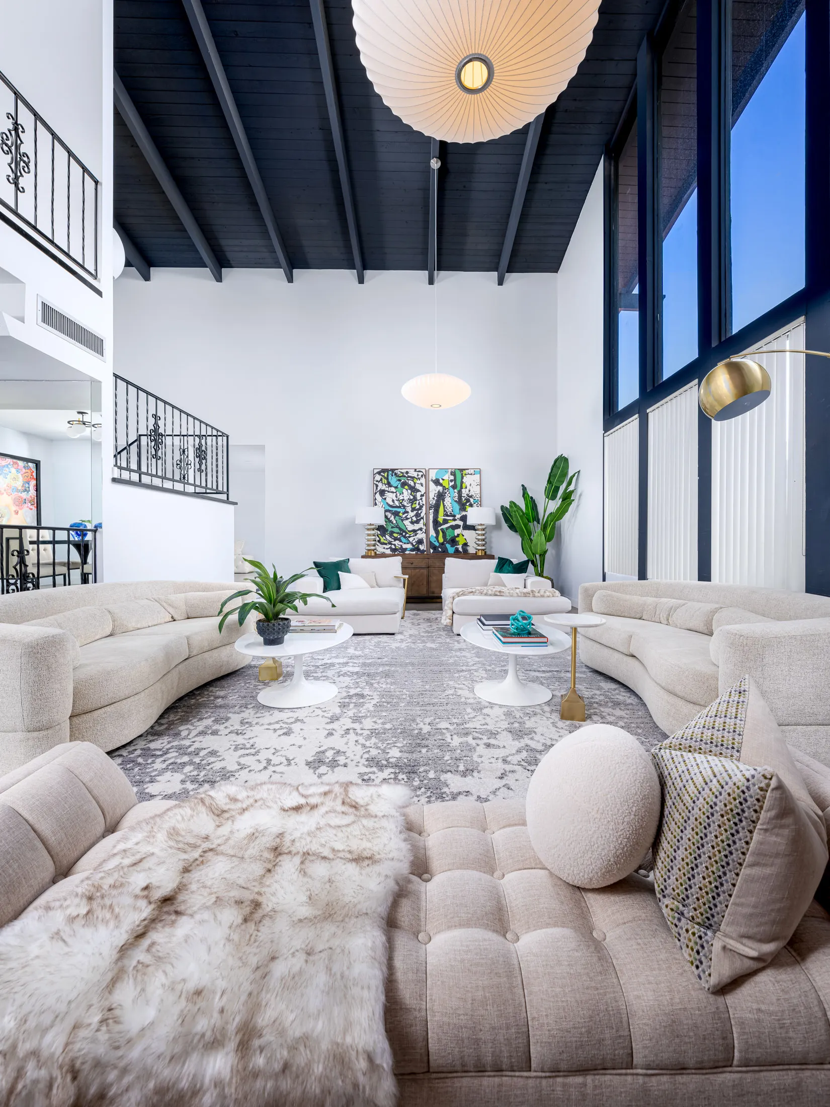 A lofty living area featuring a black vaulted ceiling, curved neutral sofas, and large abstract artwork.