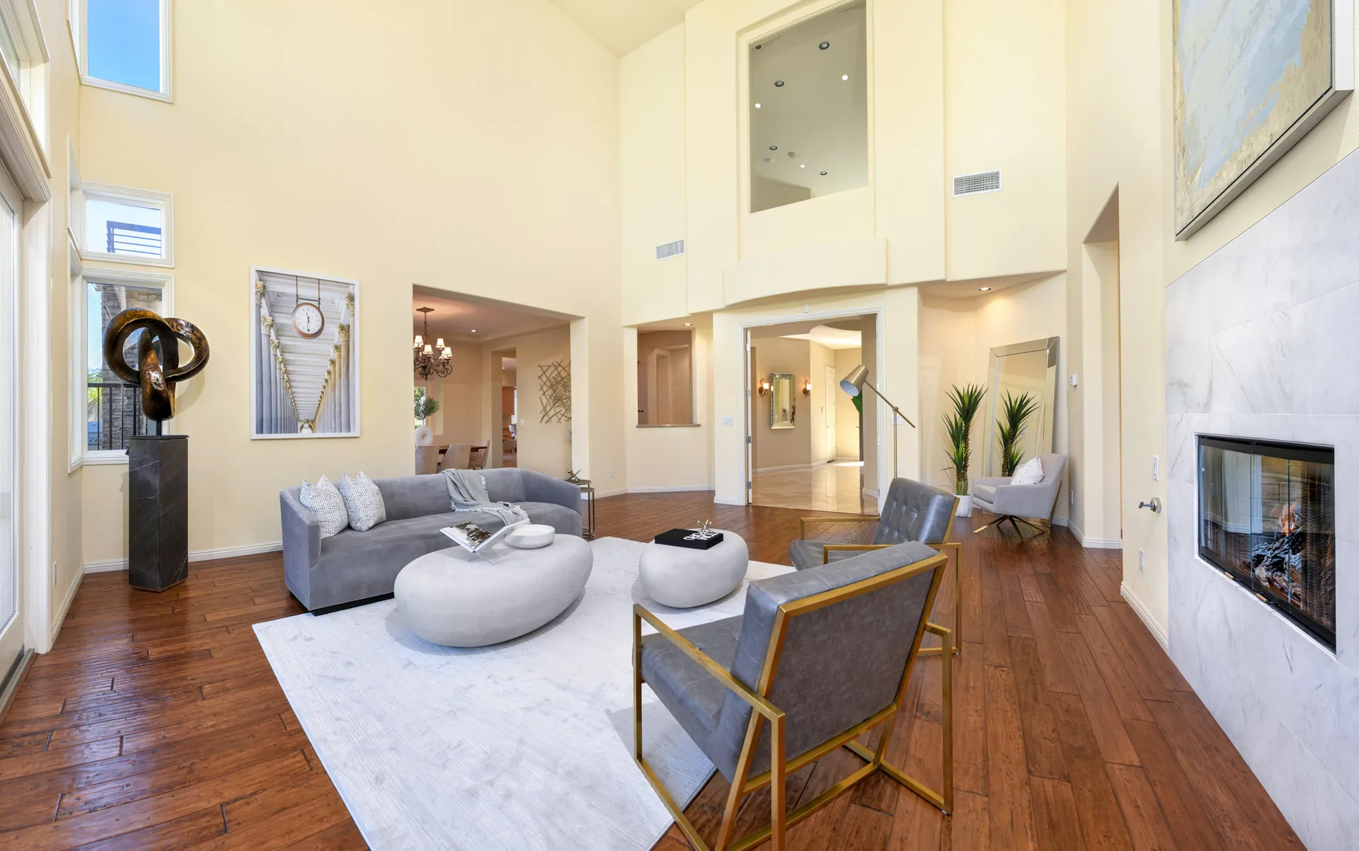 A tall living area featuring a gray curved sofa, round coffee tables, and gold-framed chairs near a white fireplace.