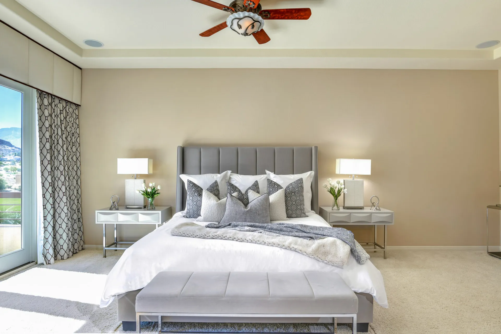 A beige-walled bedroom with a tall gray headboard, white bedding, and a bench at the foot of the bed.