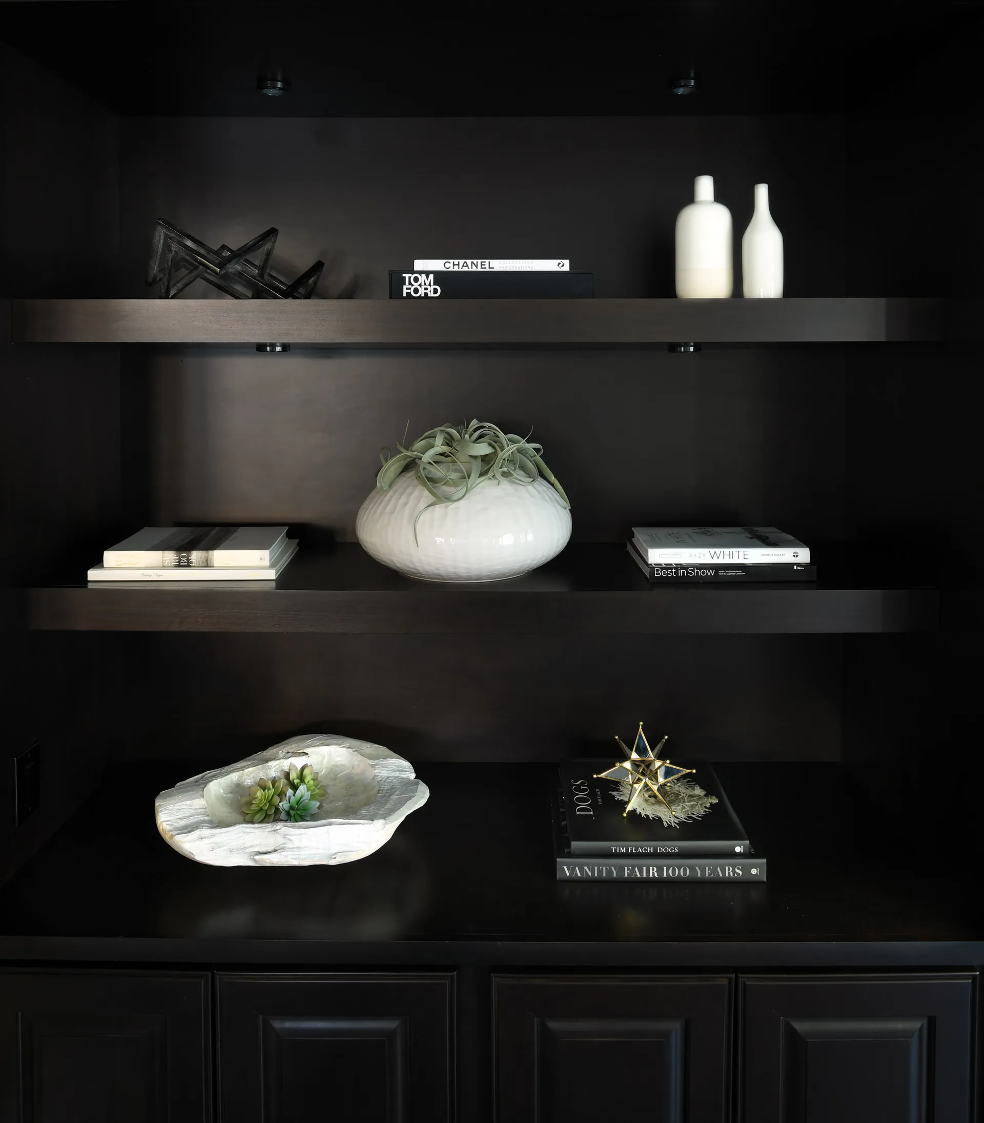 Dark built-in shelving displaying decorative books, a white ceramic vase with greenery, and accent sculptures.