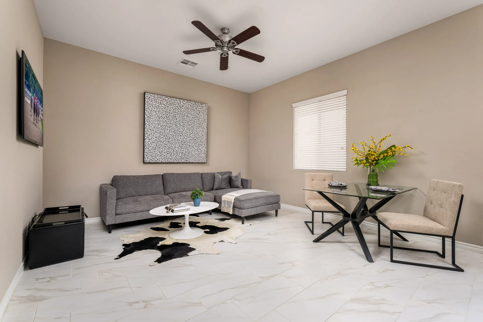 A neutral-toned living area with a gray sectional, a white coffee table, a black and white rug, and a small glass dining set.