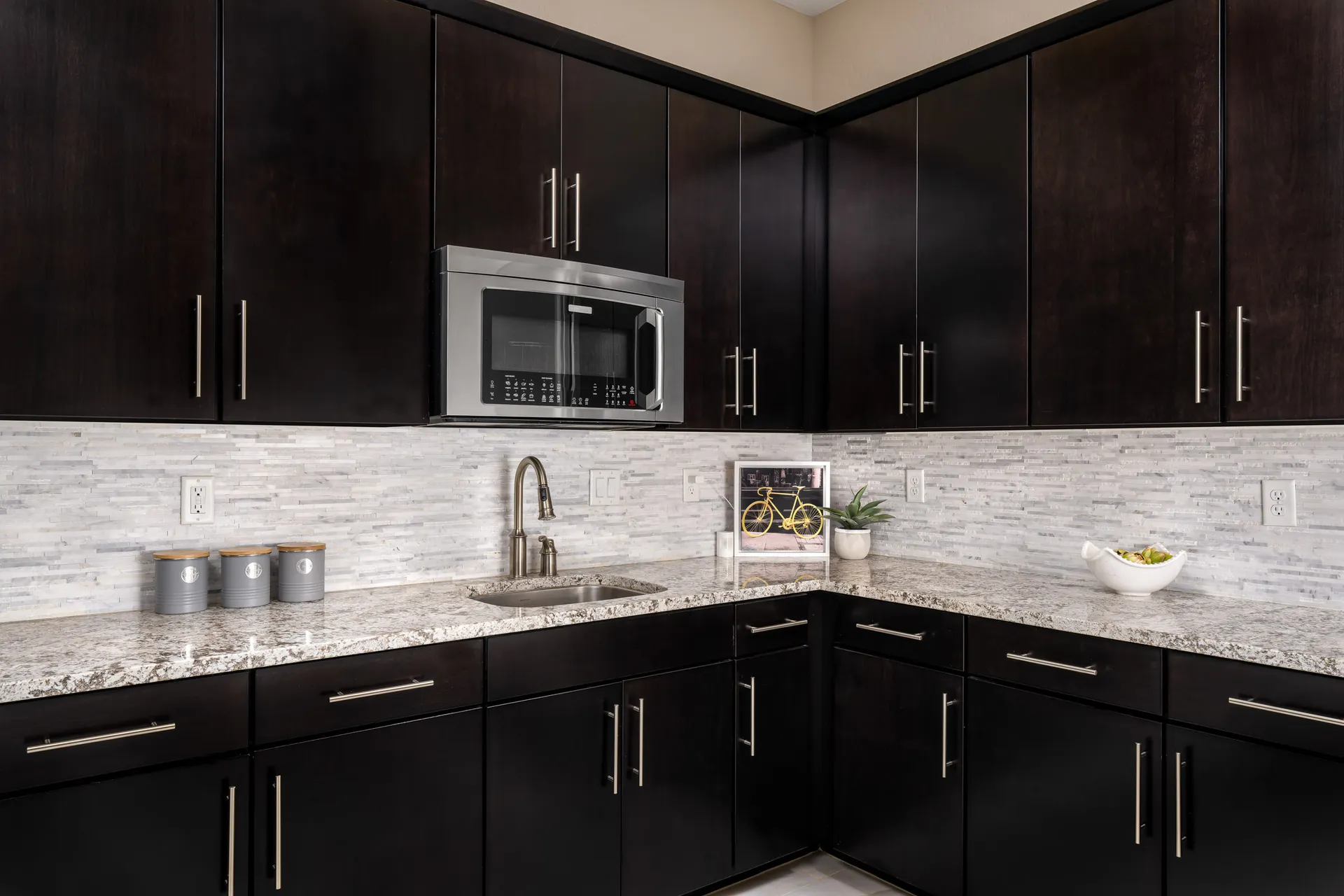 Corner view of a kitchen with dark espresso cabinets, stainless steel appliances, and a mosaic tile backsplash.