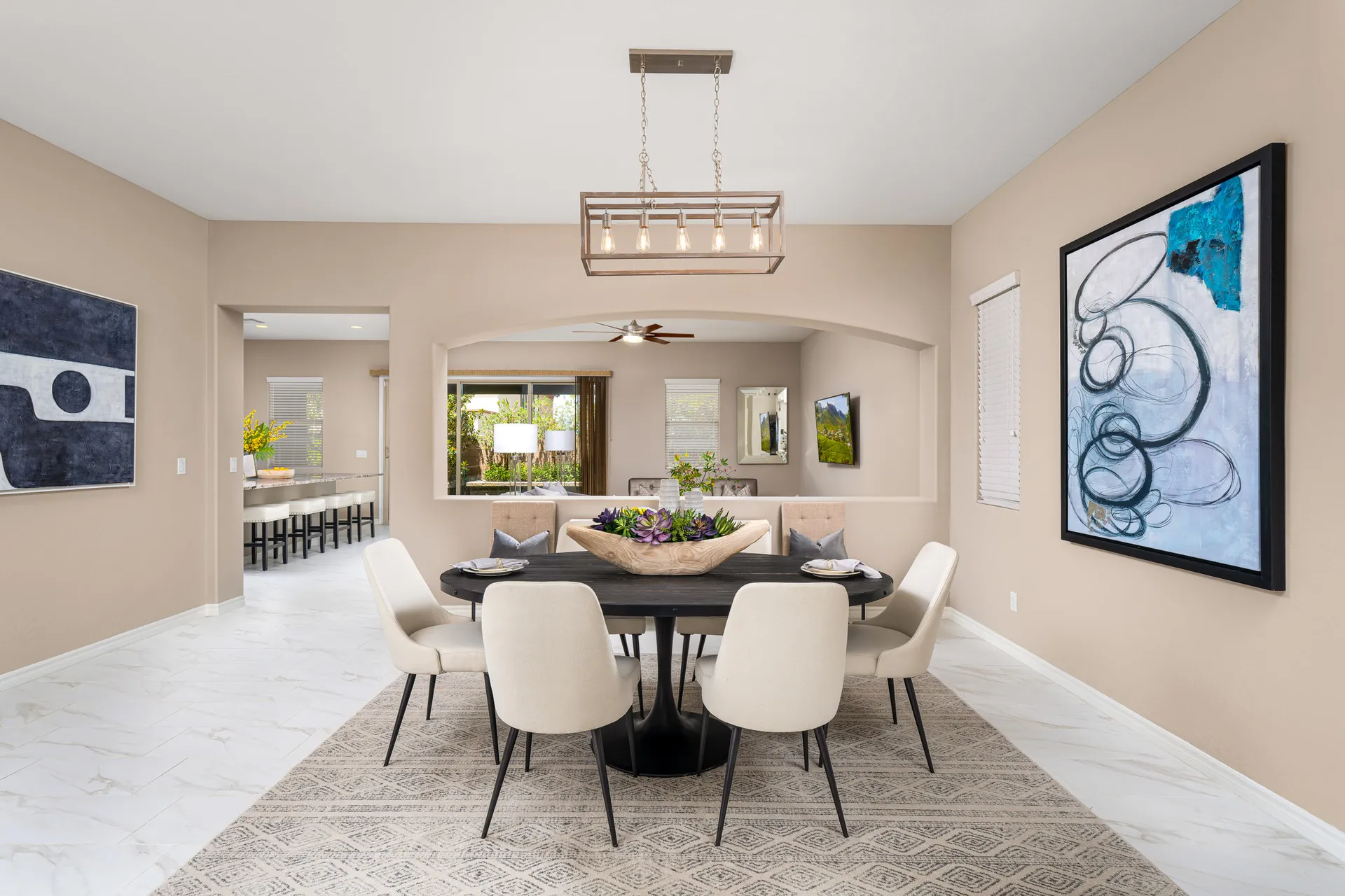 An oval black dining table with neutral chairs, a succulent centerpiece, and large abstract art in a bright open room.