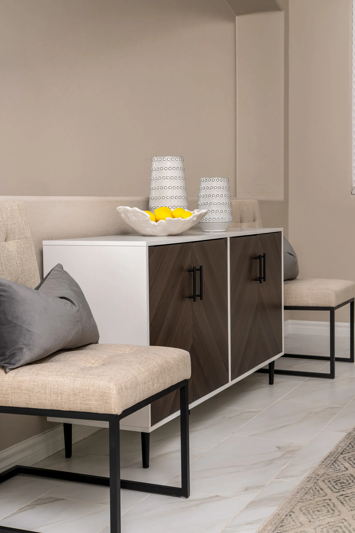A white and wood sideboard with two patterned doors, topped with decorative vases and a bowl of lemons.