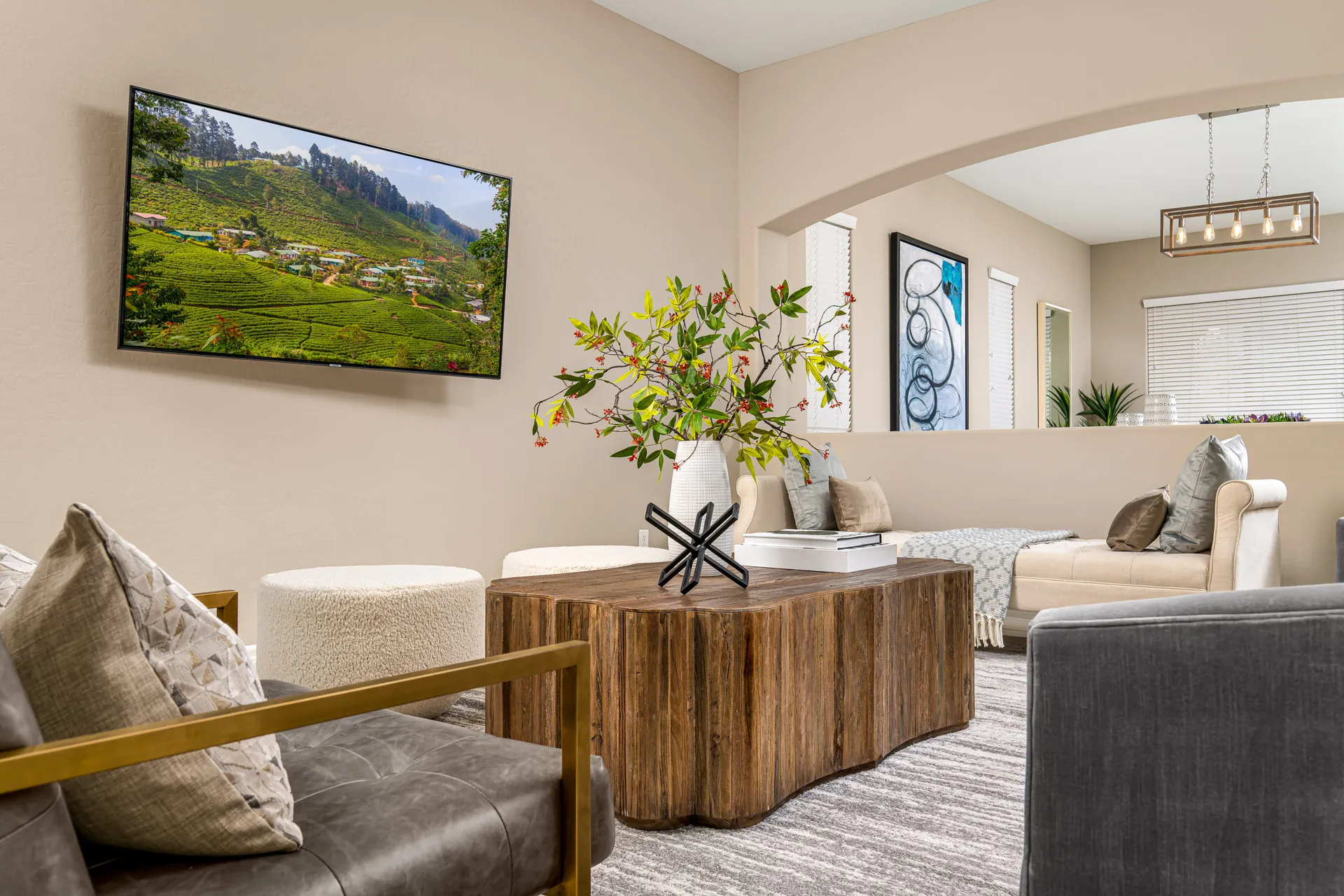A living space featuring a sculptural wood coffee table, ivory chaise, and decorative greenery near a mounted television.