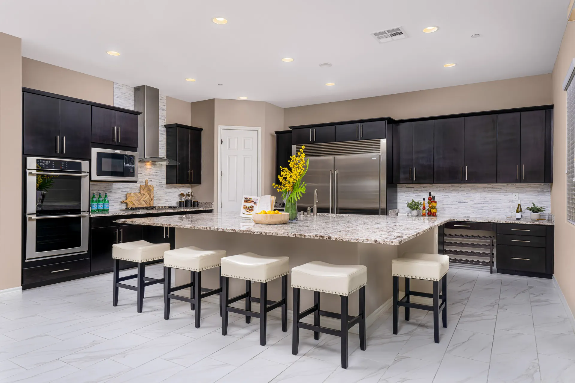 A modern kitchen featuring dark cabinetry, stainless steel appliances, and a large granite island with bar stools.