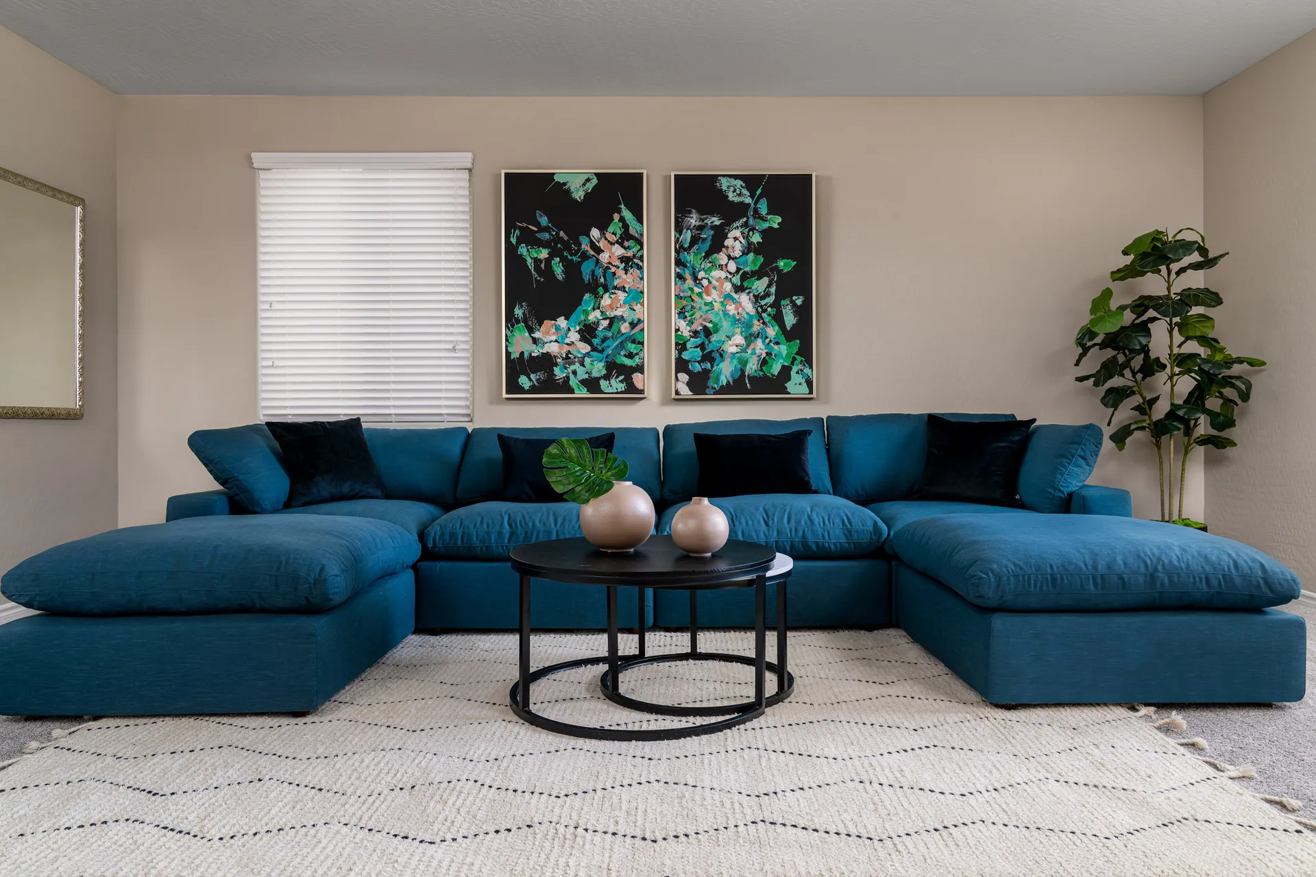 A large teal sectional sofa with black round coffee tables and two abstract art pieces on the wall.