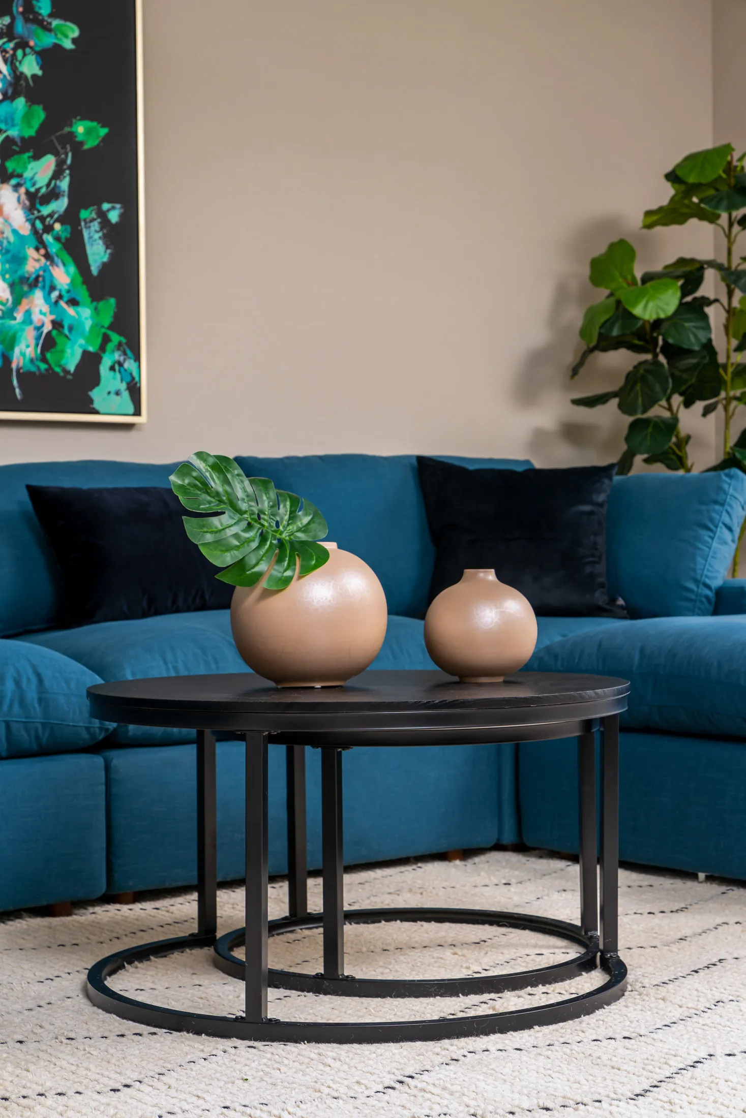 A close-up of black round coffee tables holding beige spherical vases in front of a teal sectional sofa.