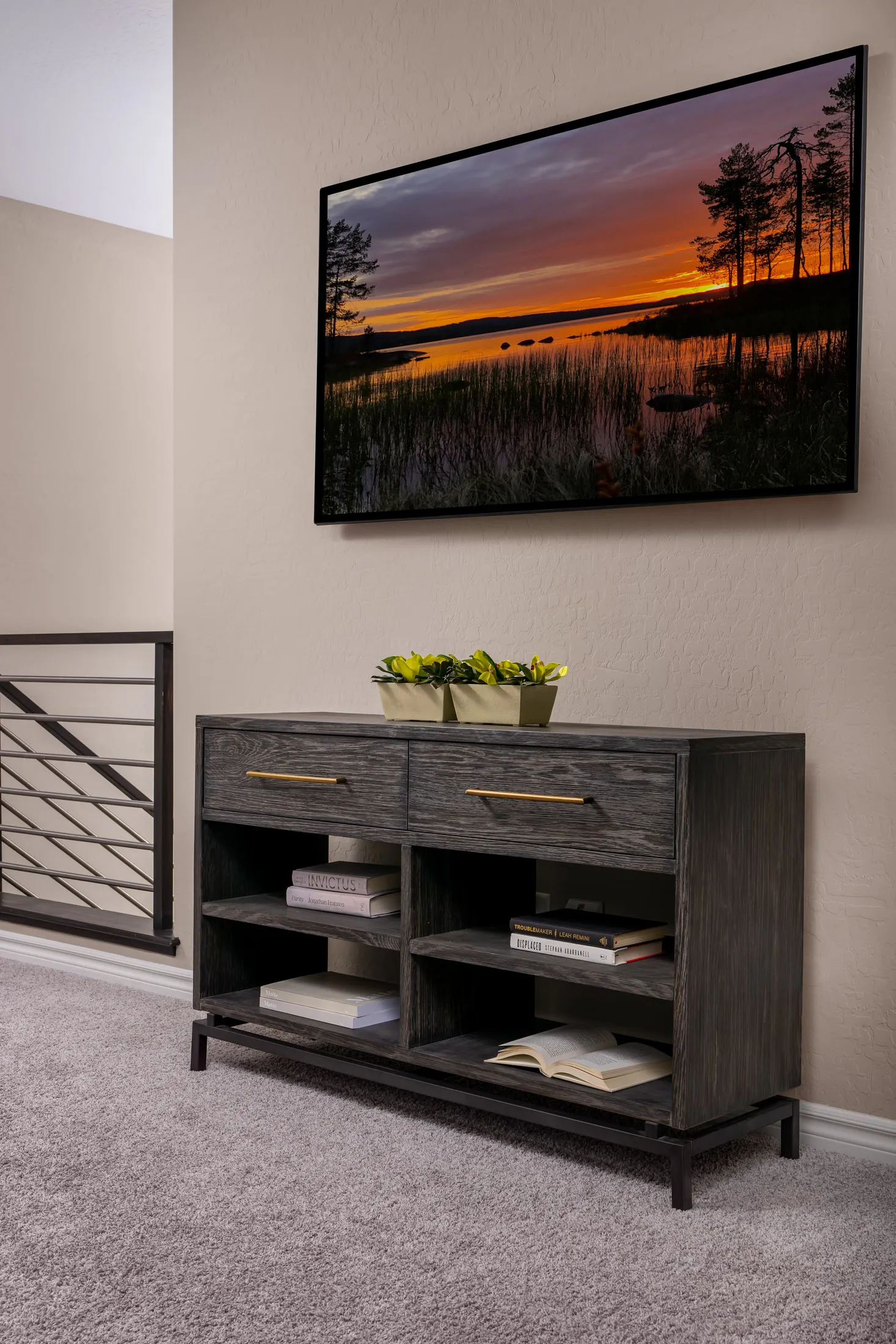 A dark wood console with gold handles beneath a wall-mounted TV displaying a sunset scene.