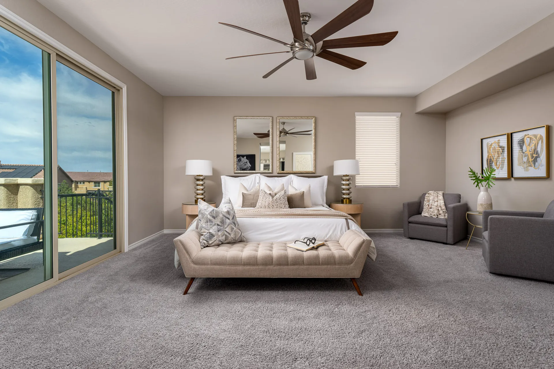 A spacious bedroom with a neutral color palette, tufted bench, white bedding, and large sliding doors leading to a balcony.