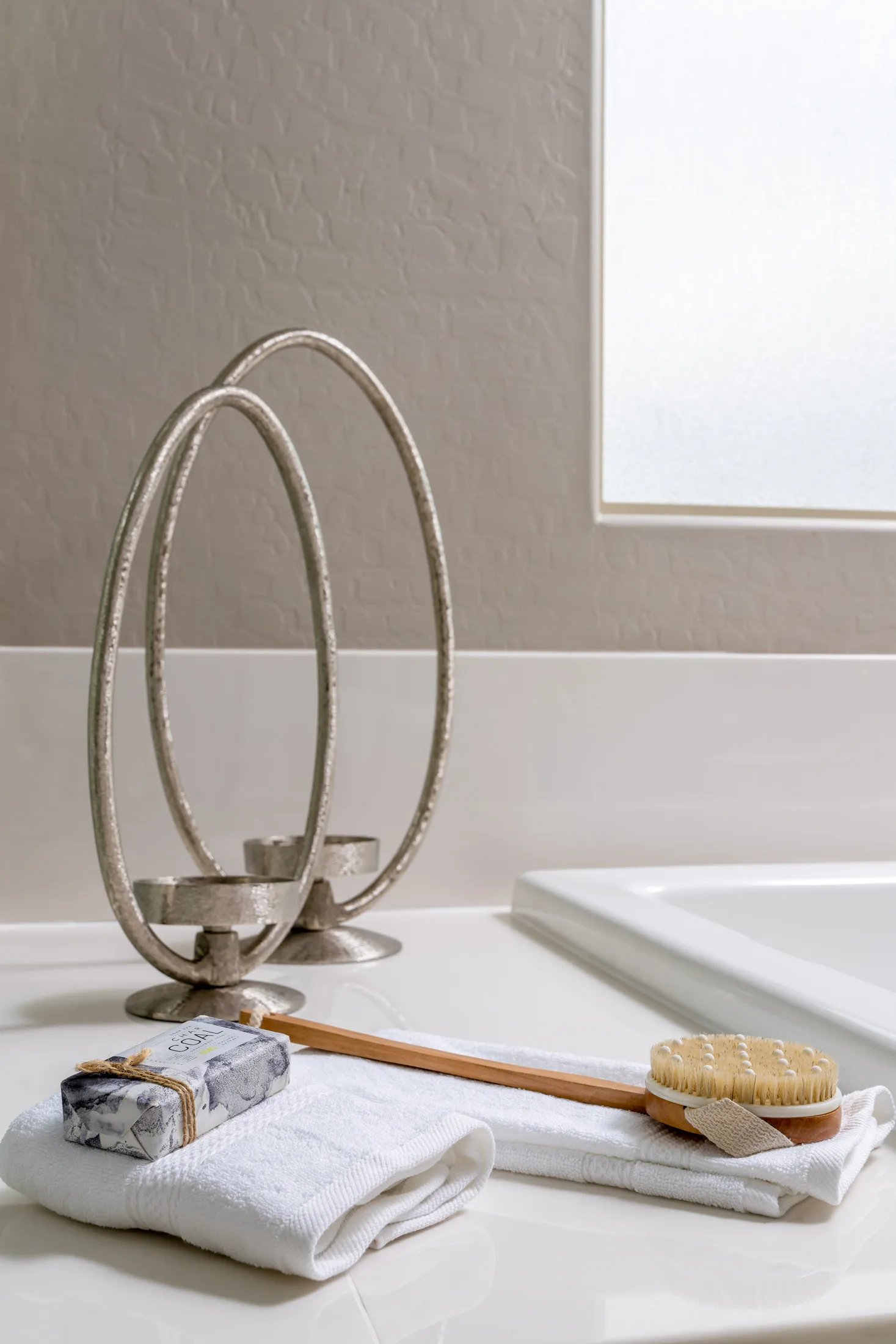 A bathroom countertop featuring white towels, a wooden brush, and a modern metal candle holder.